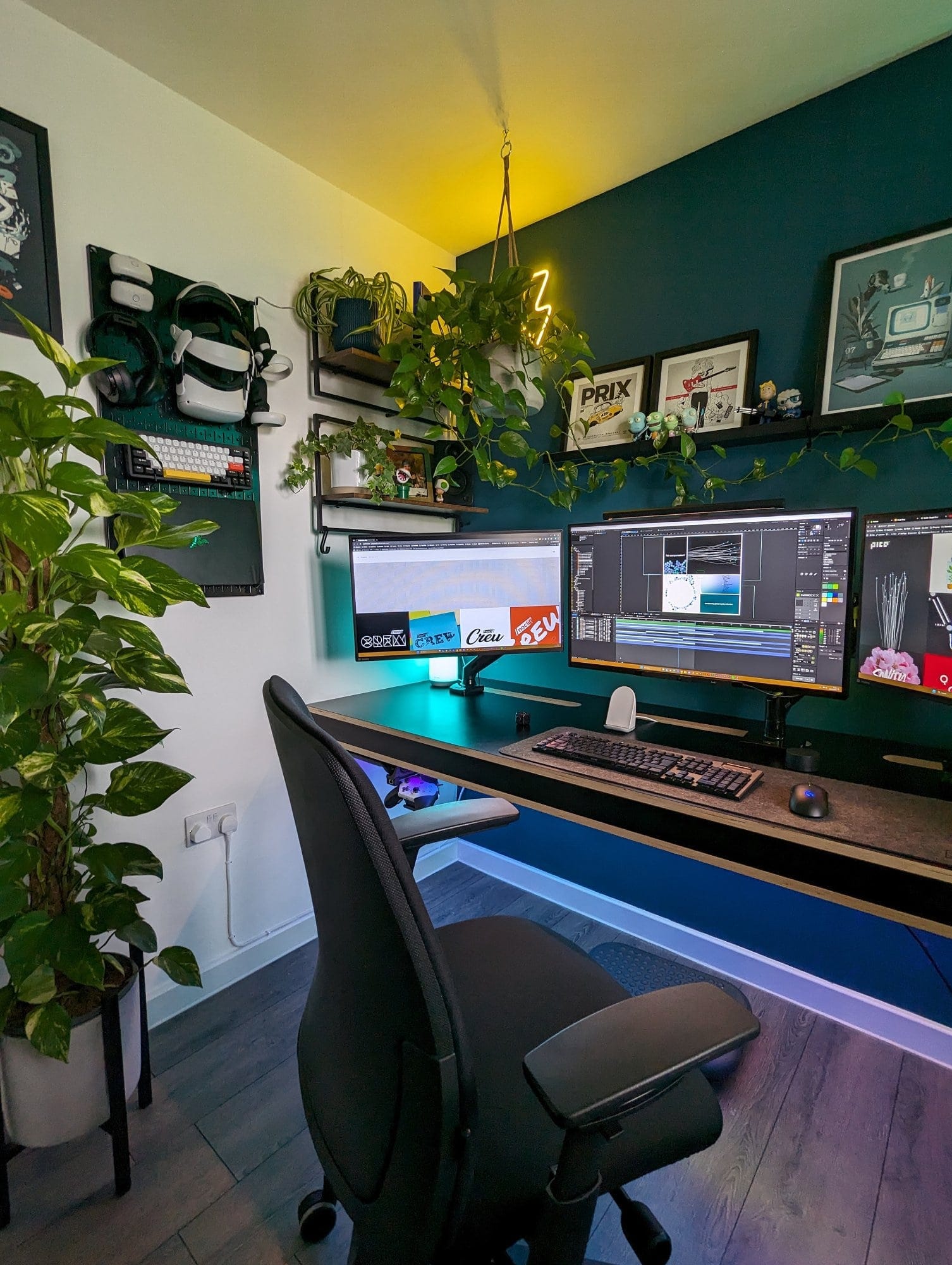 A battlestation with a multi-monitor desk setup, featuring an ergonomic chair, tech accessories, framed artwork, motivational posters, and ambient LED lighting