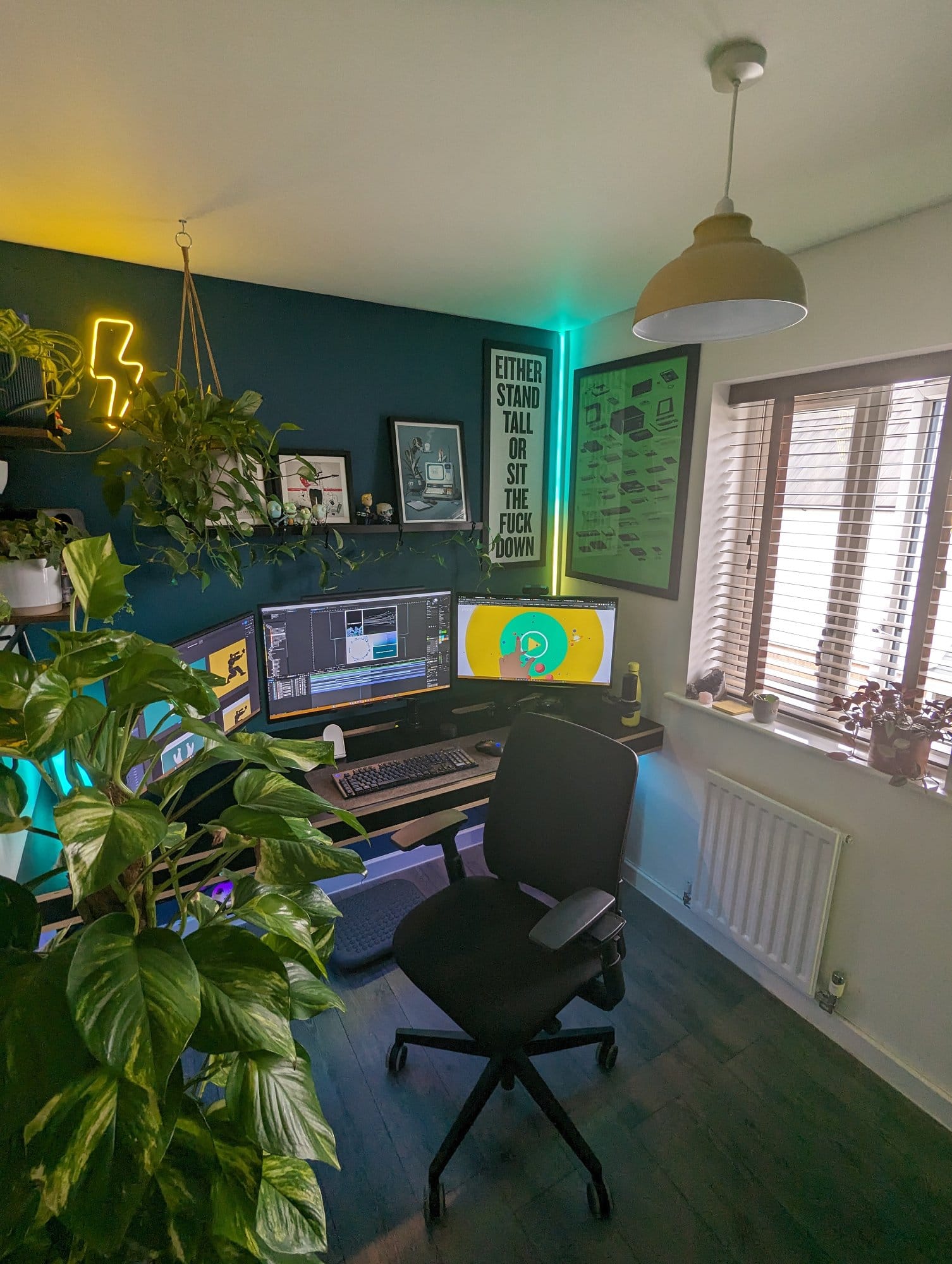 A stylish home office featuring multiple monitors on a desk, accentuated by vibrant green plants, motivational wall art, and modern lighting