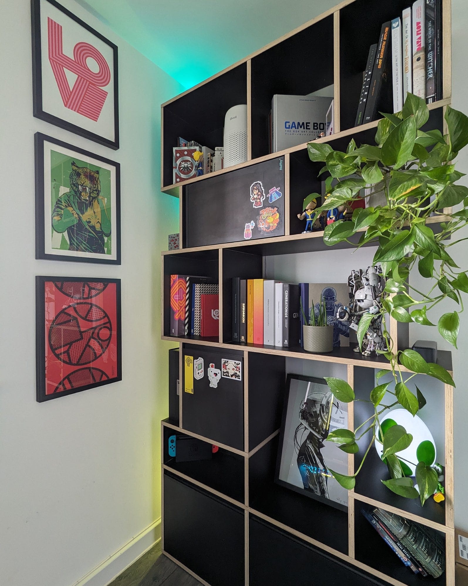 A Tylko shelving unit in a home office displaying books, collectibles, and decor items, adorned with vibrant green plants and accompanied by framed art on the adjacent wall