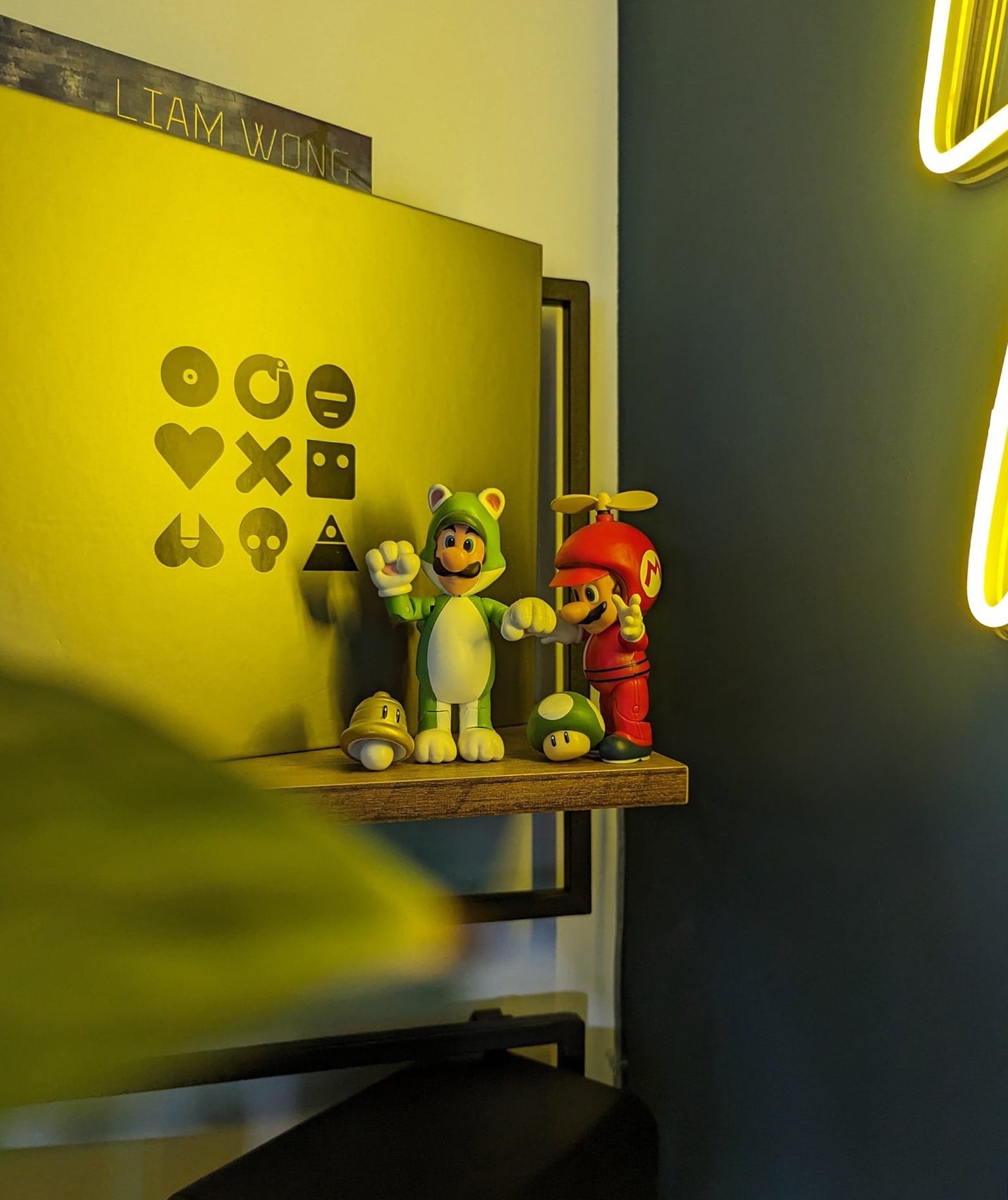 A shelf displaying Luigi and Mario action figures in special costumes from the Super Mario series, set against a backdrop with a glowing yellow light