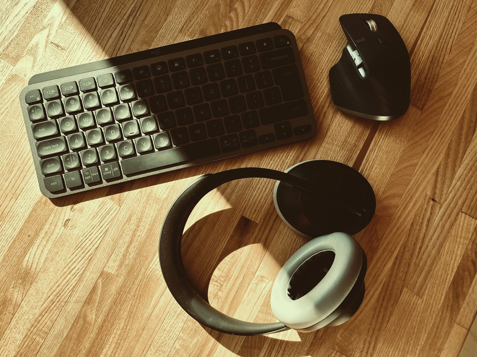 A keyboard, mouse, and headphones on a wooden desk in sunlight