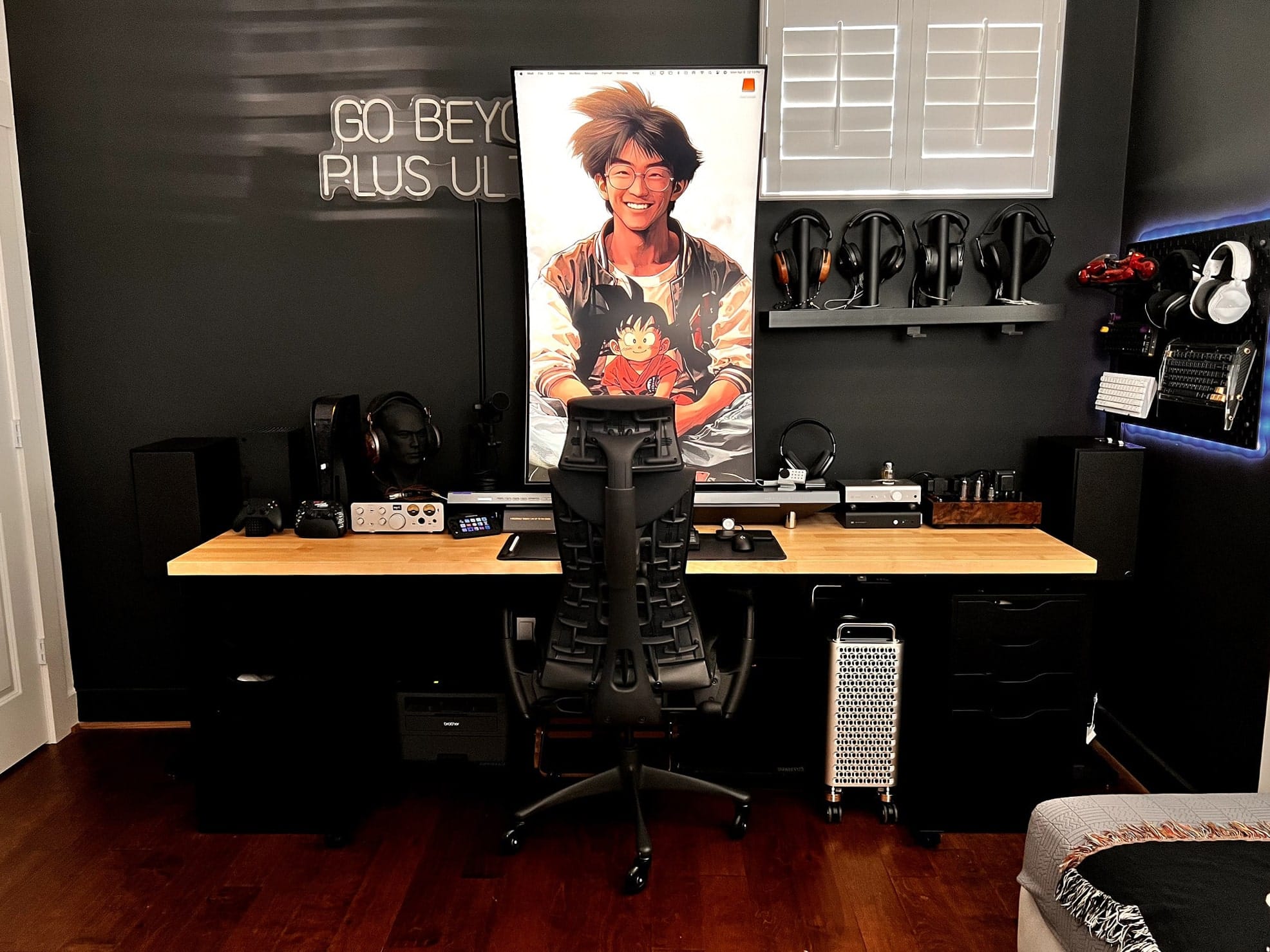 A modern gaming setup with a large curved Samsung monitor, an LED sign ”GO BEYOND PLUS ULTRA” sign, ergonomic chair, audio equipment, and wall-mounted headphones in a minimalist black and wood-themed room
