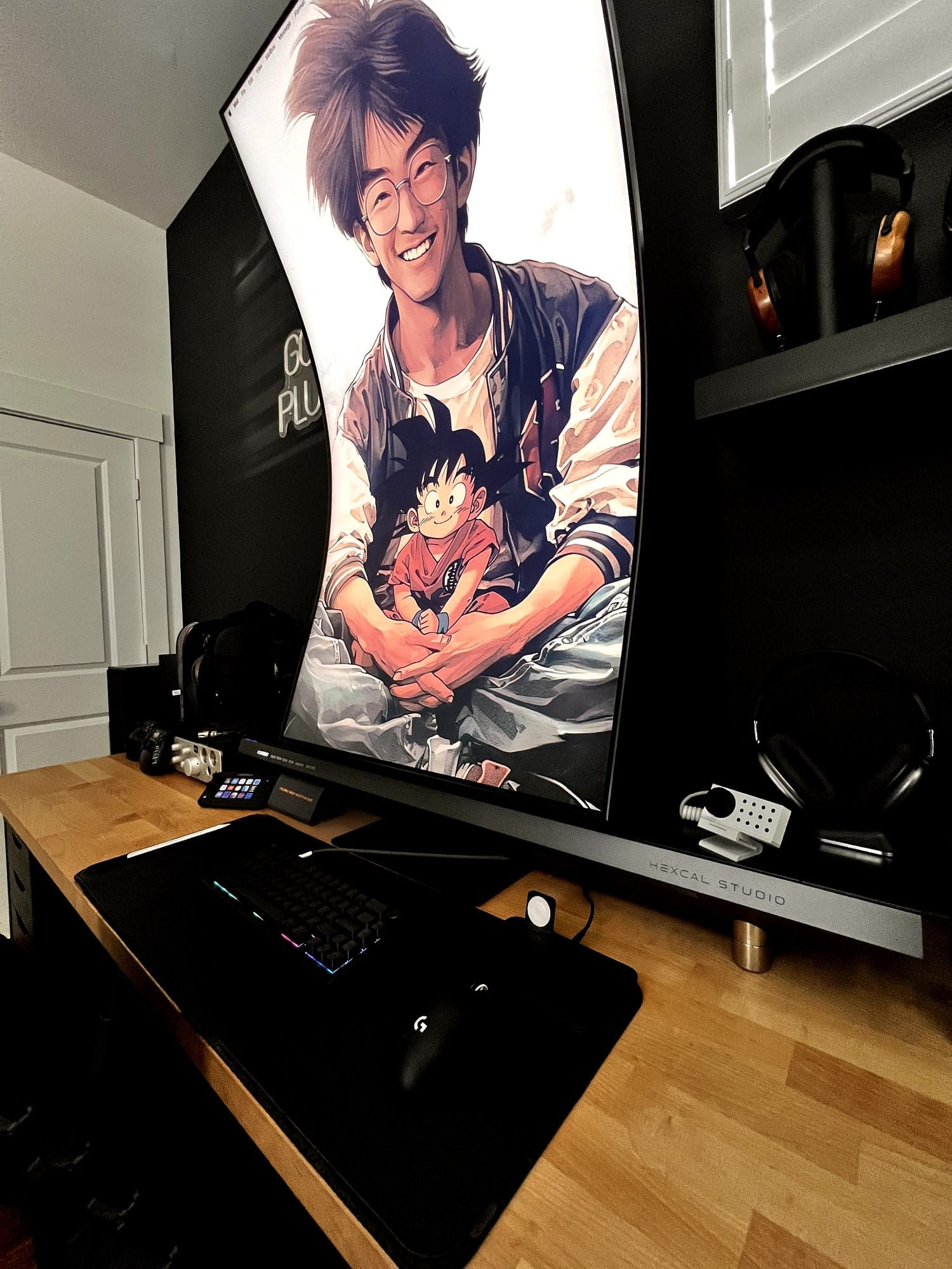 A modern gaming setup with a large curved monitor displaying an anime character, a mechanical keyboard, a gaming mouse, a Stream Deck, and headphones, all neatly arranged on a wooden desk