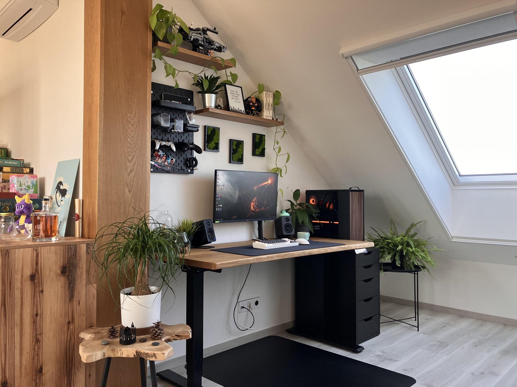 A stylish home office featuring a wooden desk with an ergonomic chair, computer setup, and multiple plants, illuminated by natural light from a large window