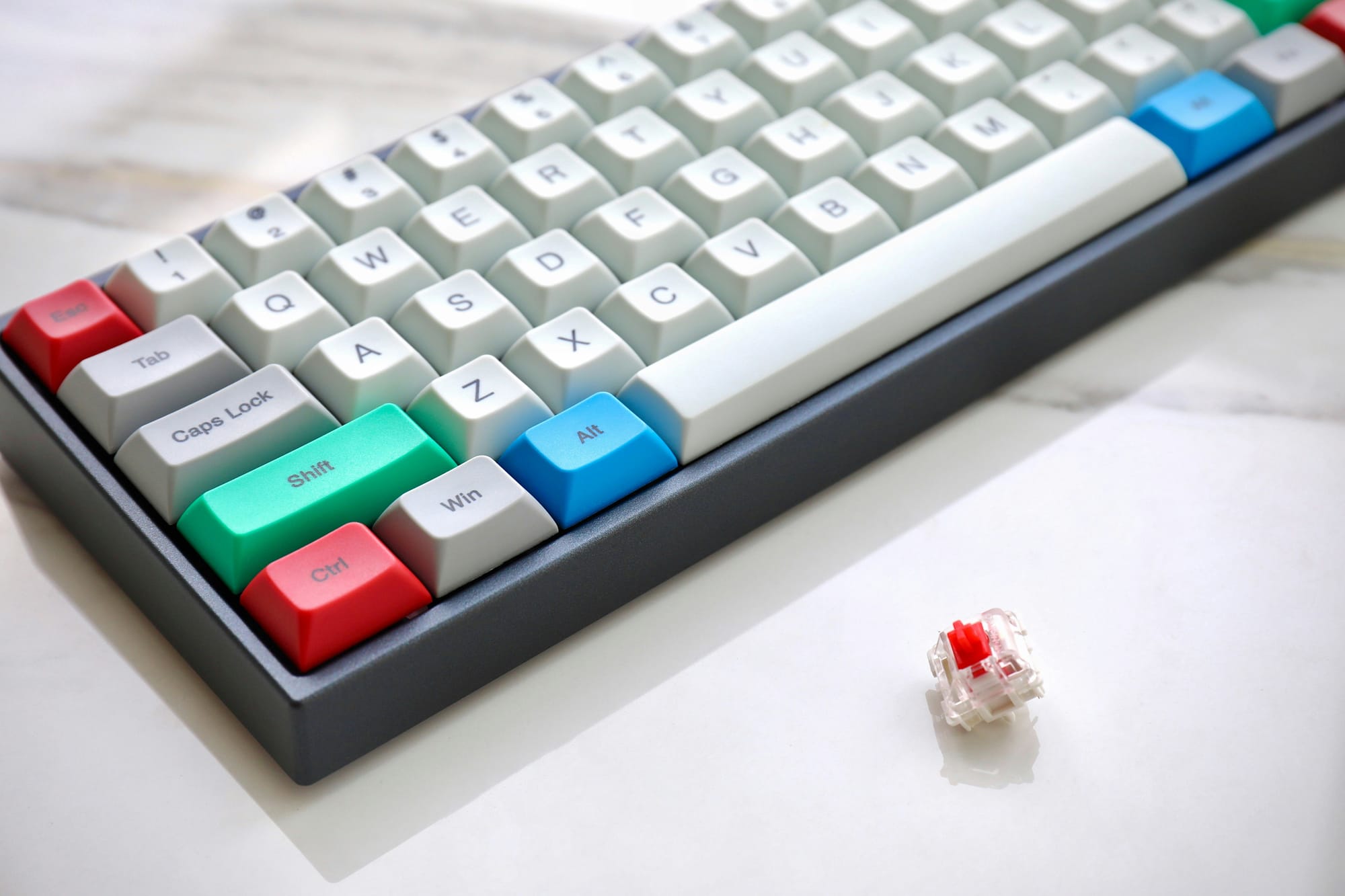 A mechanical keyboard with colourful keycaps and a red switch placed on a white marble surface