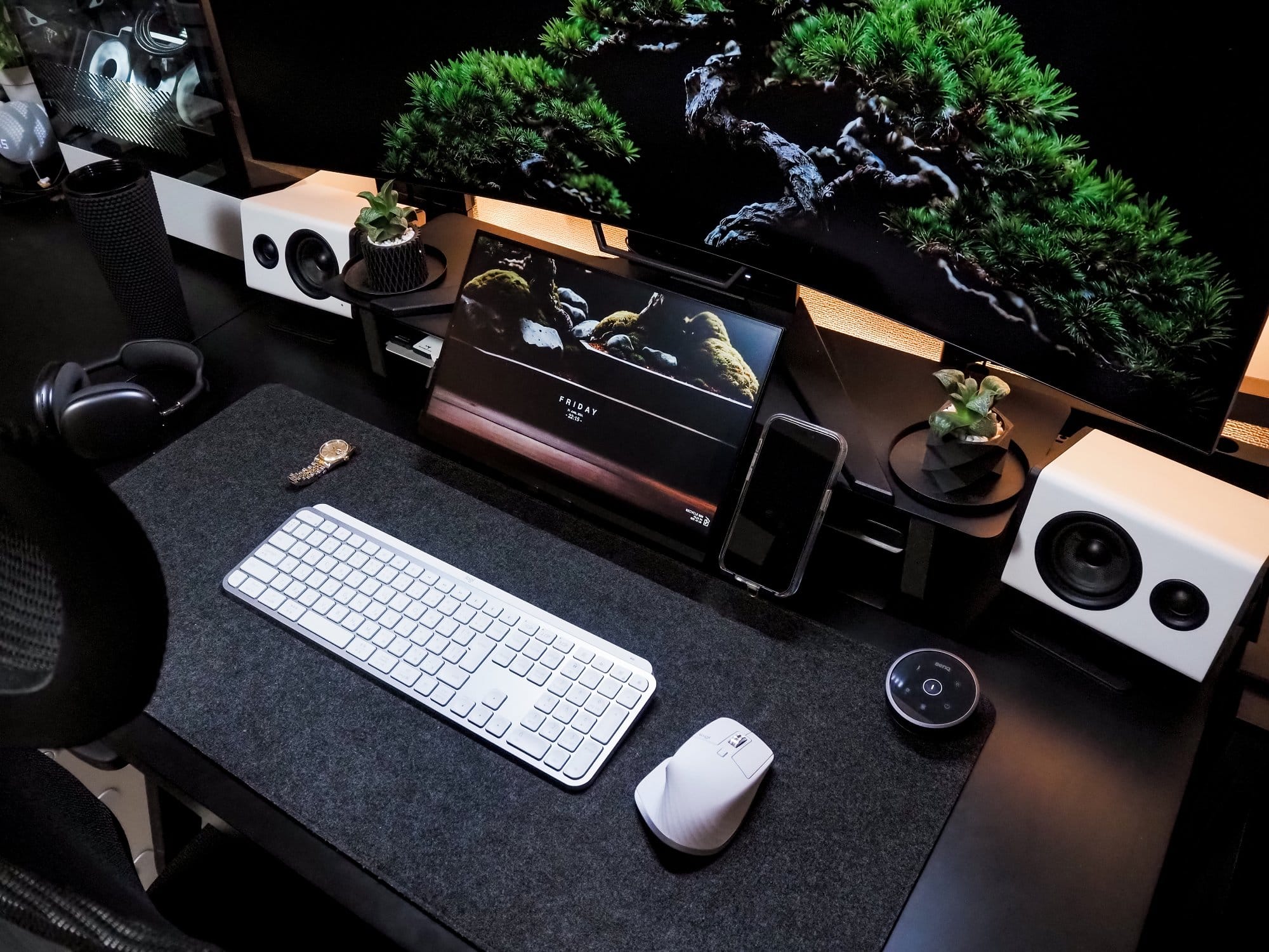 A top-down view of a meticulously arranged desk setup featuring a Logitech MX Keys S keyboard, a Logitech MX Master 3S mouse, white NZXT Relay speakers, a MacBook Pro 13-inch, M1, 2020 laptop, and bonsai trees