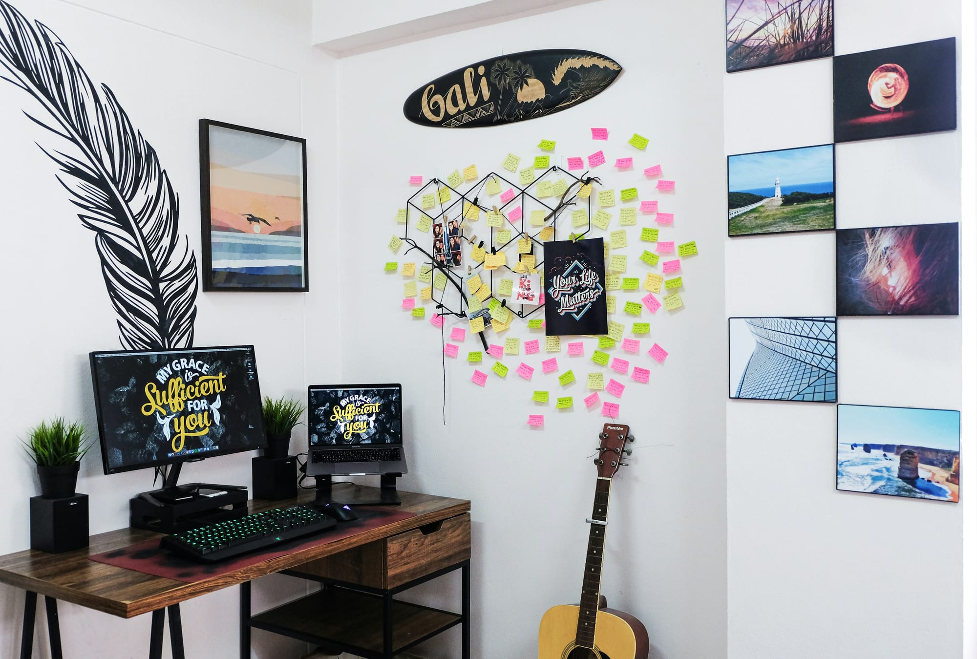 A home office with motivational posters, sticky notes on the wall, a guitar, and various decorative elements