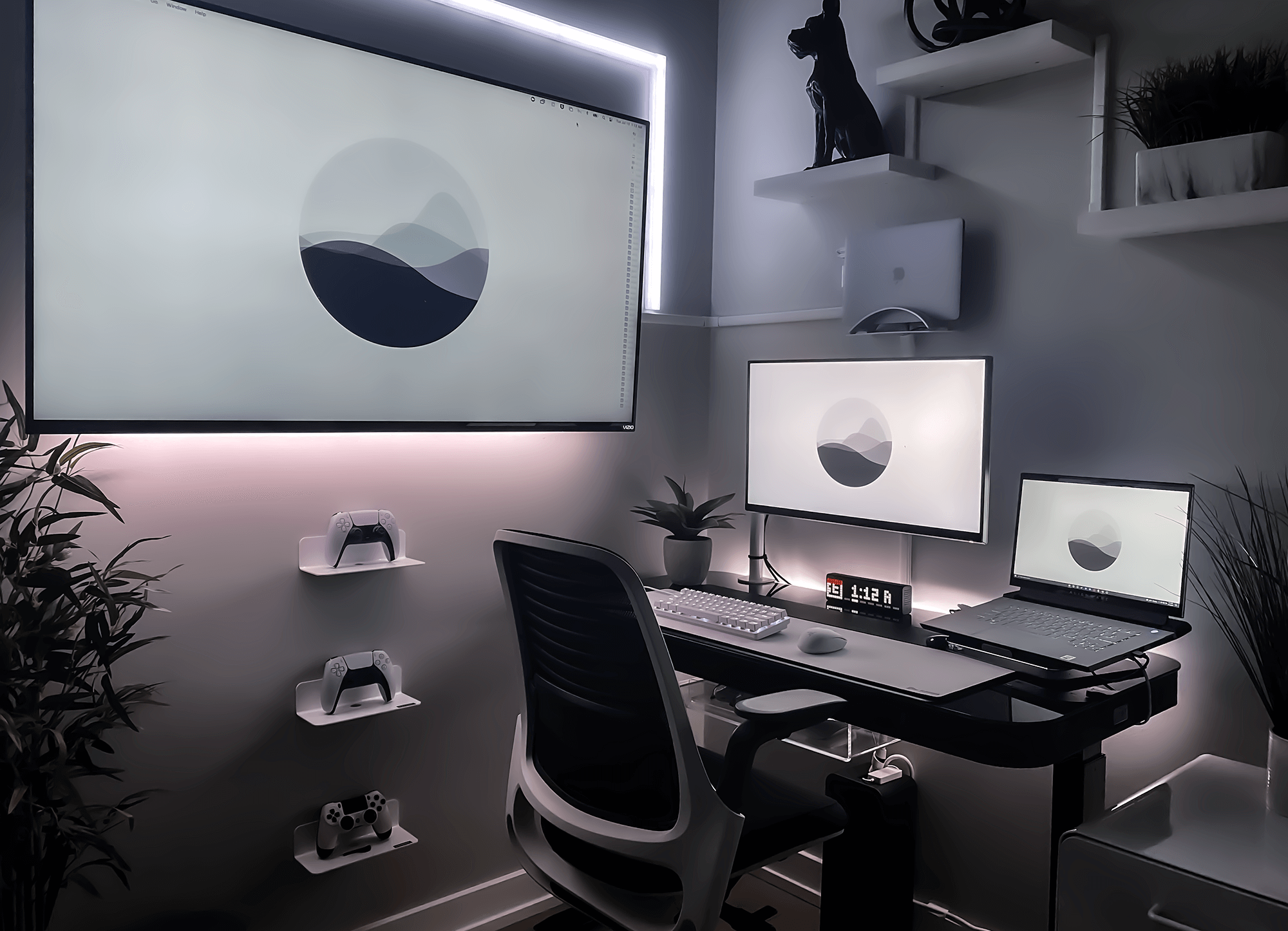 A sleek and minimalist workspace featuring a dual-monitor setup with a large wall-mounted display, a laptop on a stand, and a secondary monitor, all harmonised with a monochrome theme and accented by LED strip lighting, complemented by a modern ergonomic chair and wall-mounted shelves displaying gaming controllers