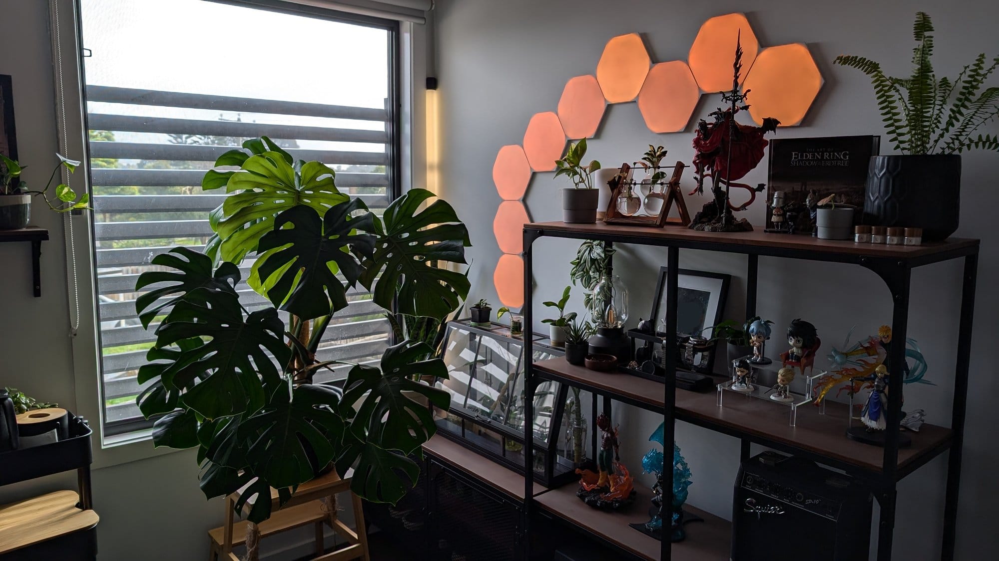 A cosy and creative corner filled with lush plants, illuminated by hexagonal wall lights, showcasing a mix of figurines, books, and personal items on stylish shelves