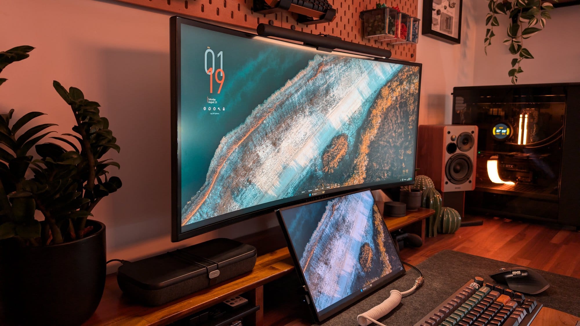 A cosy and sophisticated home workspace featuring an Alienware (AW3420DW) monitor paired with a 15″ portable monitor, both displaying a serene landscape, complemented by warm ambient lighting, Edifier R1280DB speakers, and a custom-built PC