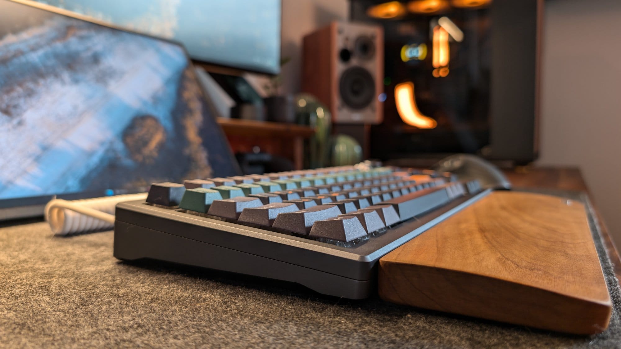 A close-up of a mechanical keyboard with colourful keycaps, paired with a wooden wrist rest, set on a felt desk mat