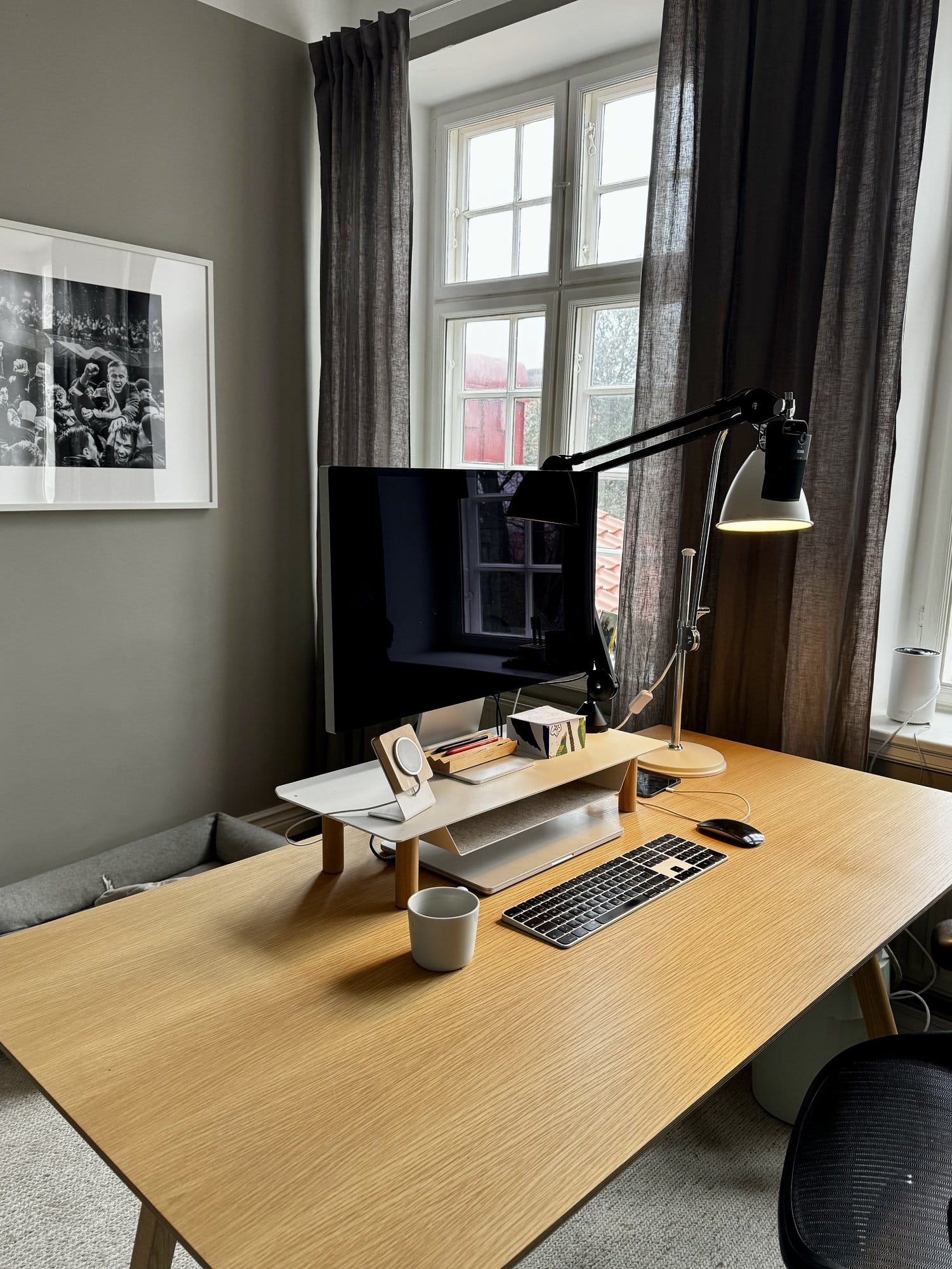 A neatly arranged desk setup with an Apple Studio Display on a Gather by Ugmonk monitor stand, paired with an Apple Keyboard and a Bestlite BL1 desk lamp