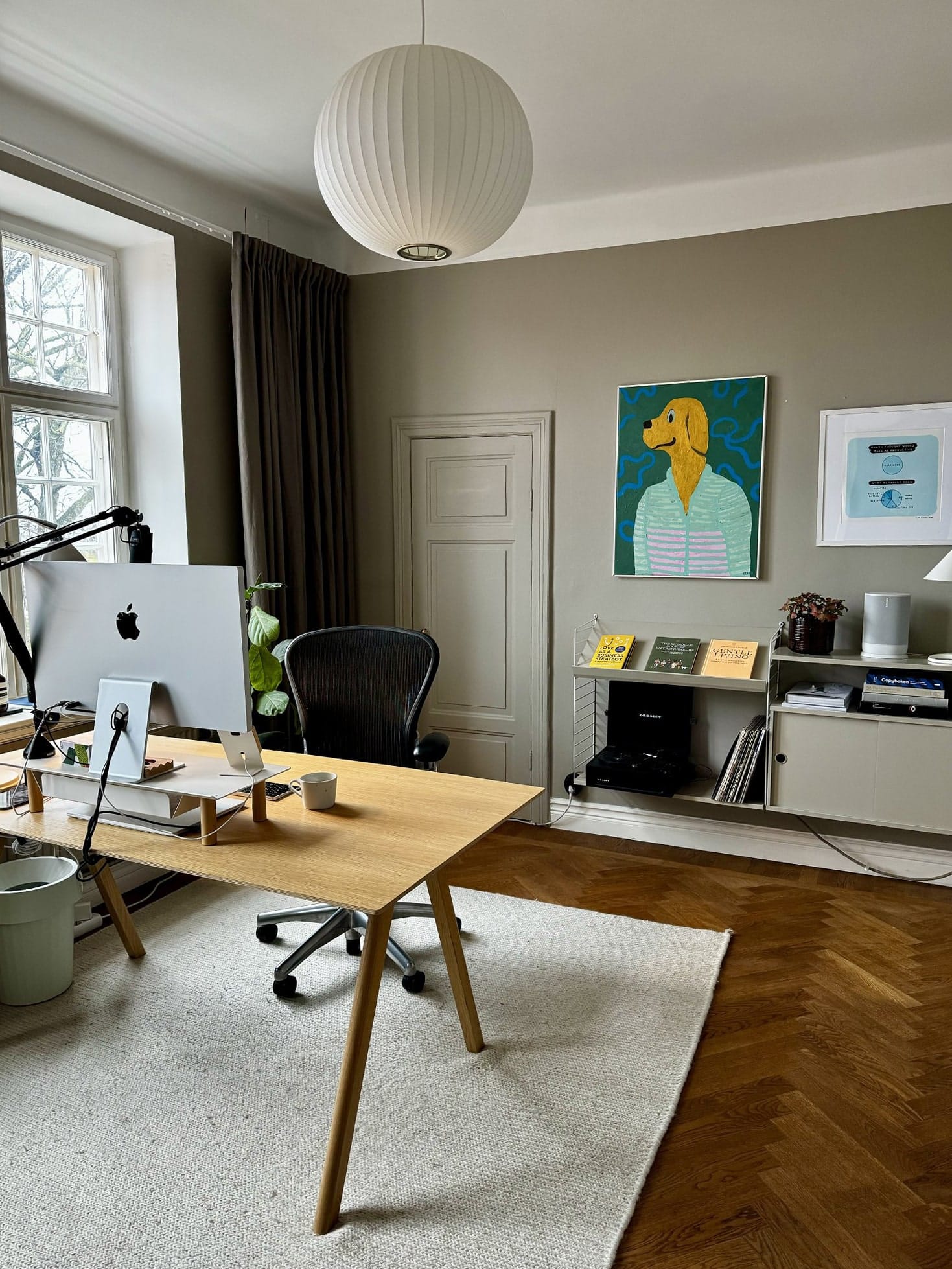 A modern home office featuring an Apple Studio Display on a Gather by Ugmonk monitor stand, a Herman Miller Aeron chair, and a MacBook Air 15″ 2024