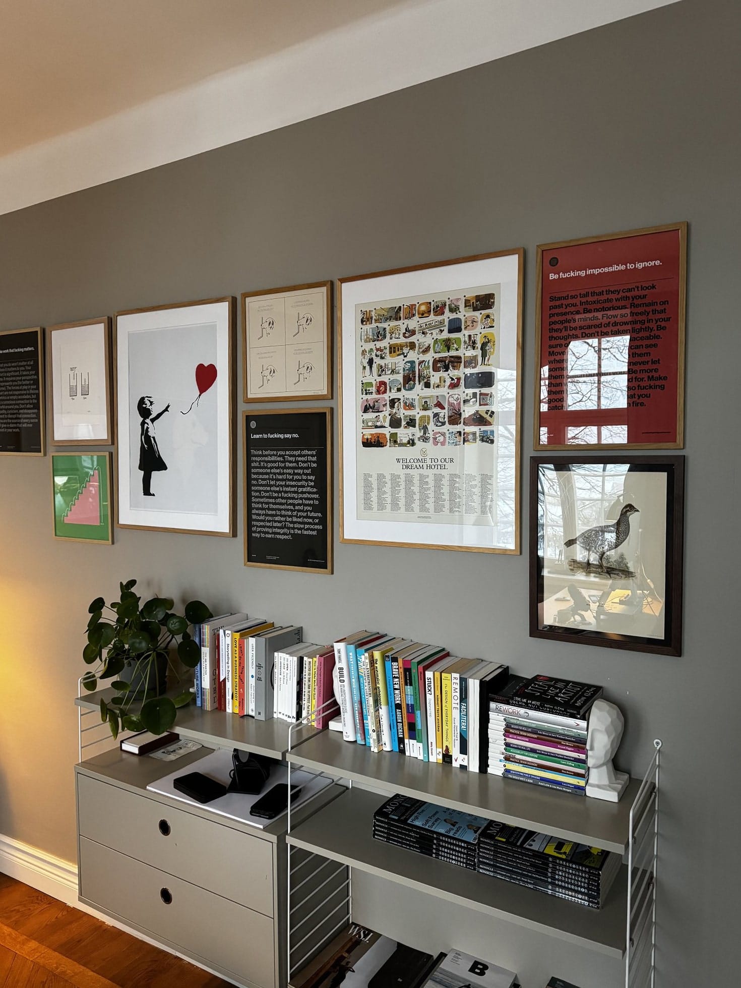 A home office with framed artwork on the wall, a bookshelf filled with books, and a desk with neatly arranged gadgets