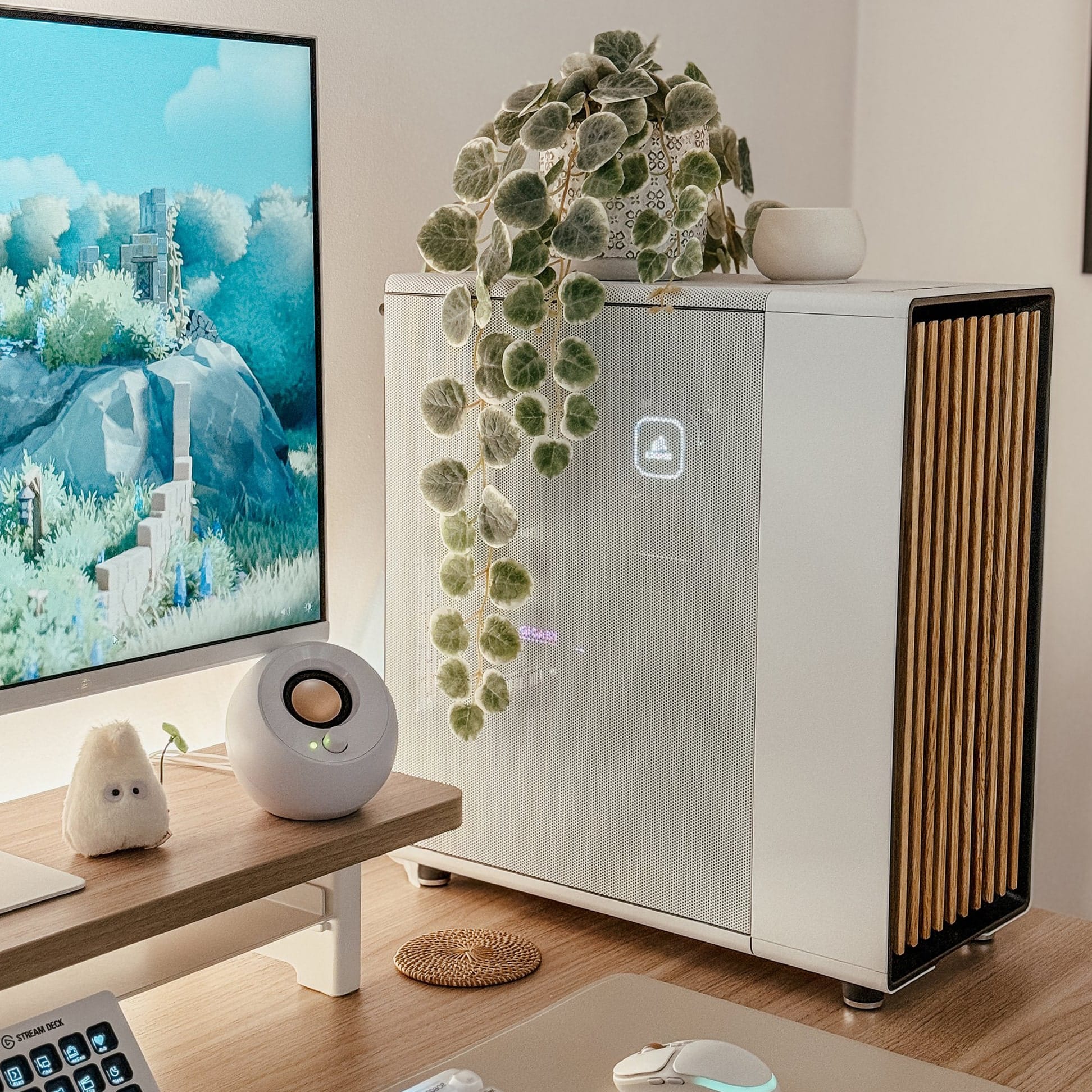 A clean and modern desk setup featuring a Samsung M7 monitor and Creative Pebble speakers, with a North by Fractal PC tower elegantly adorned with a cascading plant, all set on a Vernal-UK standing desk