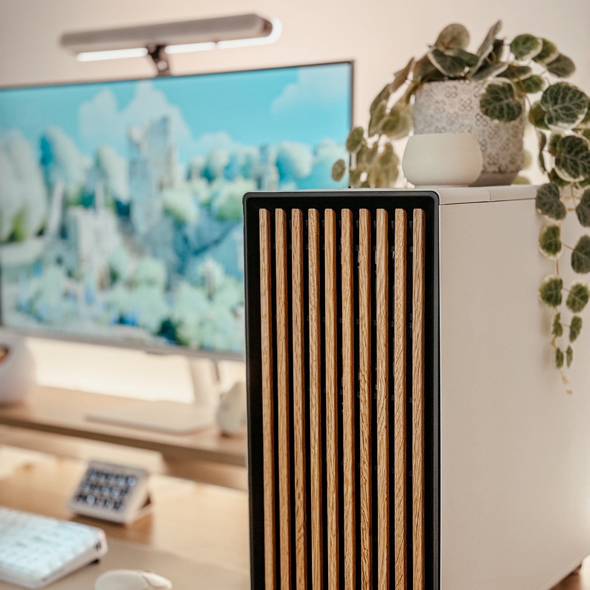 A stylish and modern workspace featuring a close-up of a North by Fractal PC tower with wooden panel accents, set against the backdrop of a Samsung M7 monitor, with decorative plants adding a touch of greenery to the minimalist setup