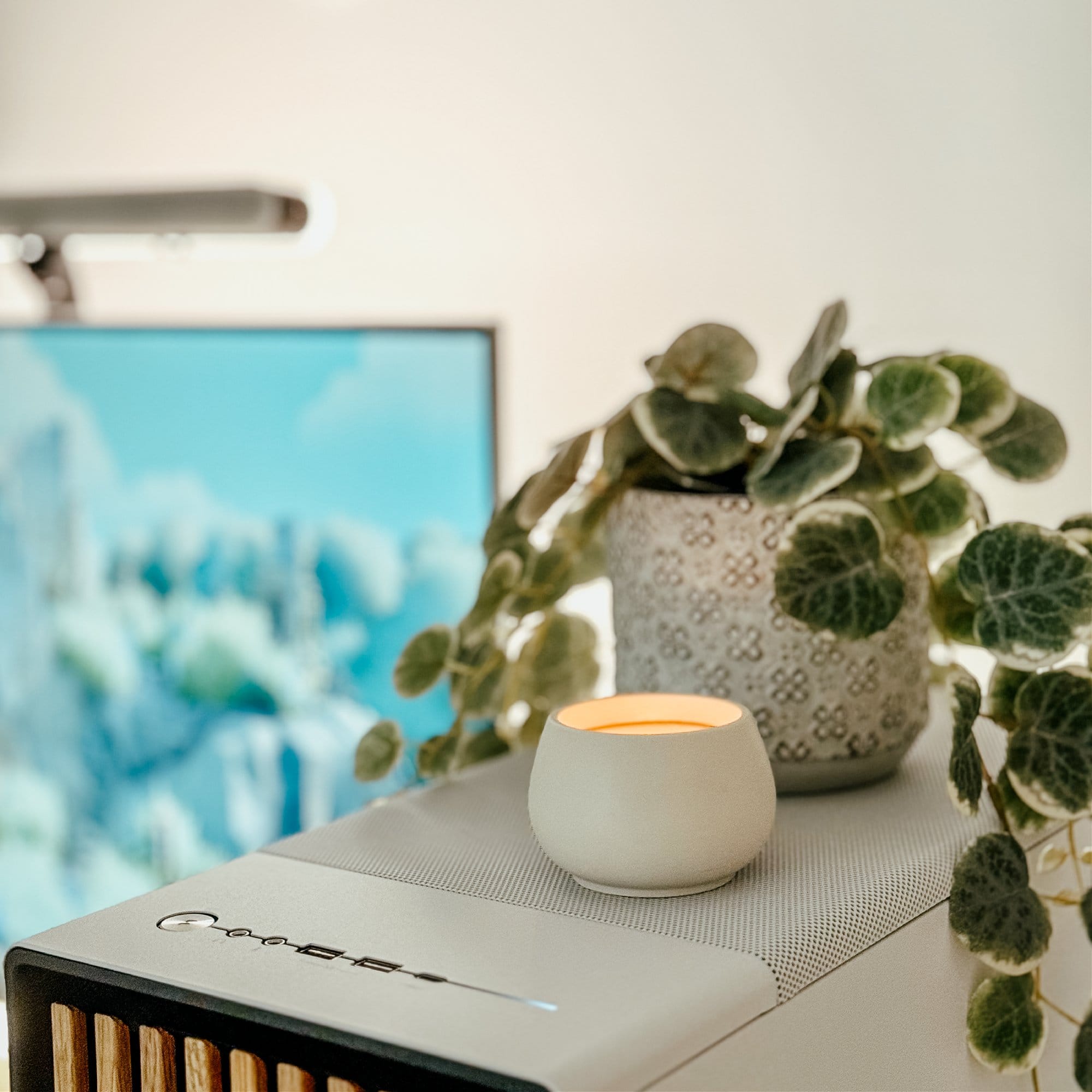 A stylish workspace featuring a North by Fractal PC tower, topped with a decorative plant and a small candle, with a Samsung M7 monitor subtly visible in the background