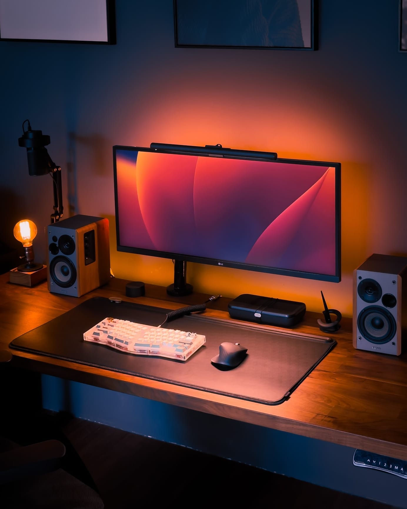 A warm-lit desk setup featuring a mechanical keyboard, an LG monitor, and wooden speakers on a wood-toned IKEA KARLBY desk