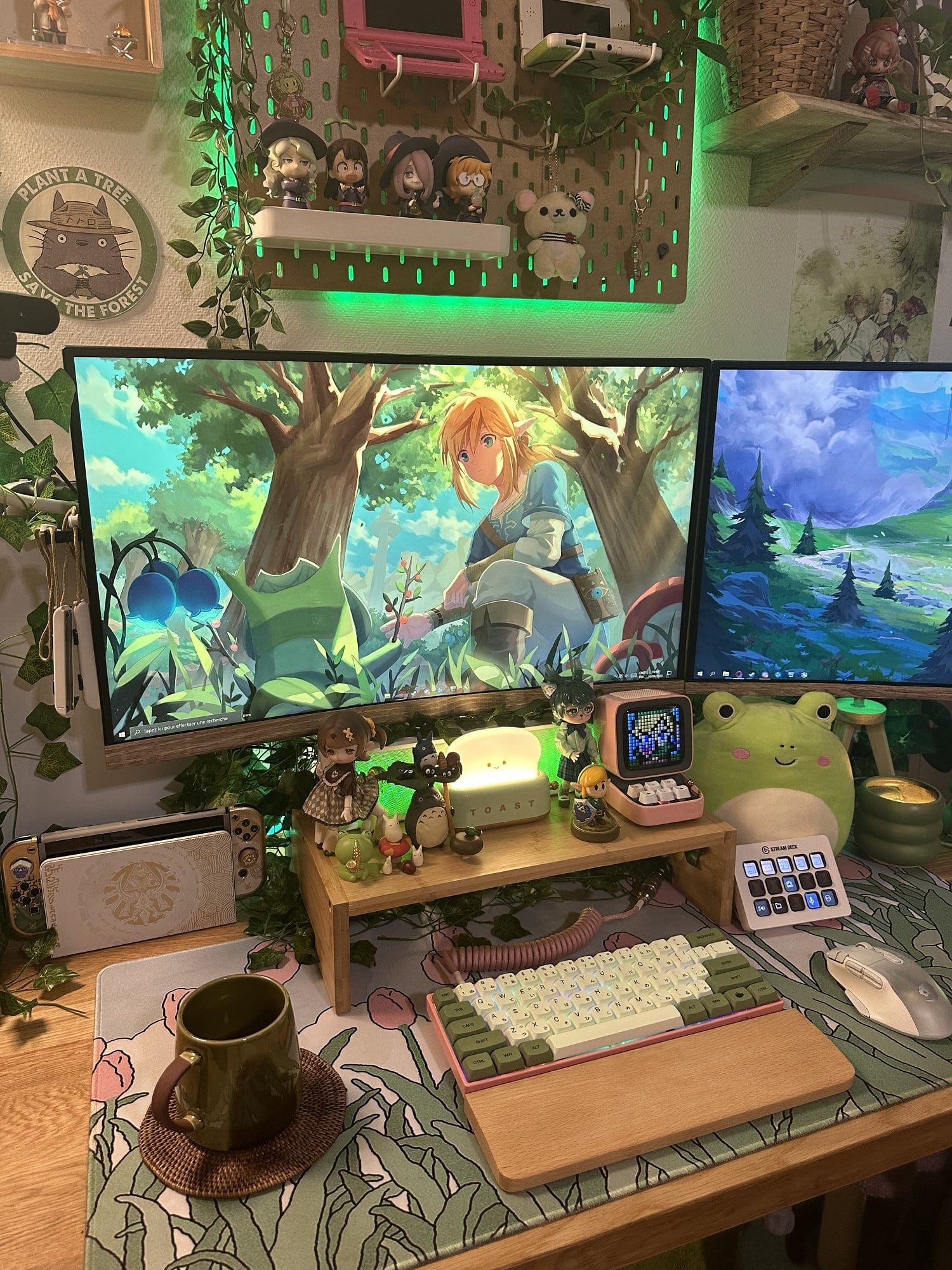 A cosy and vibrant gaming setup featuring a large monitor displaying a scene from “The Legend of Zelda,“ accompanied by a custom keyboard, all set on a nature-themed desk mat with various figurines and decorations