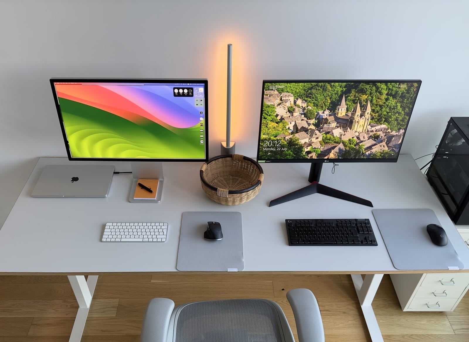 A top-down view of a minimalist desk setup featuring an Apple Studio Display and an LG UltraGear monitor, accompanied by a MacBook Pro M2 Max, a Logitech G915 TKL gaming keyboard, and a Herman Miller Aeron chair