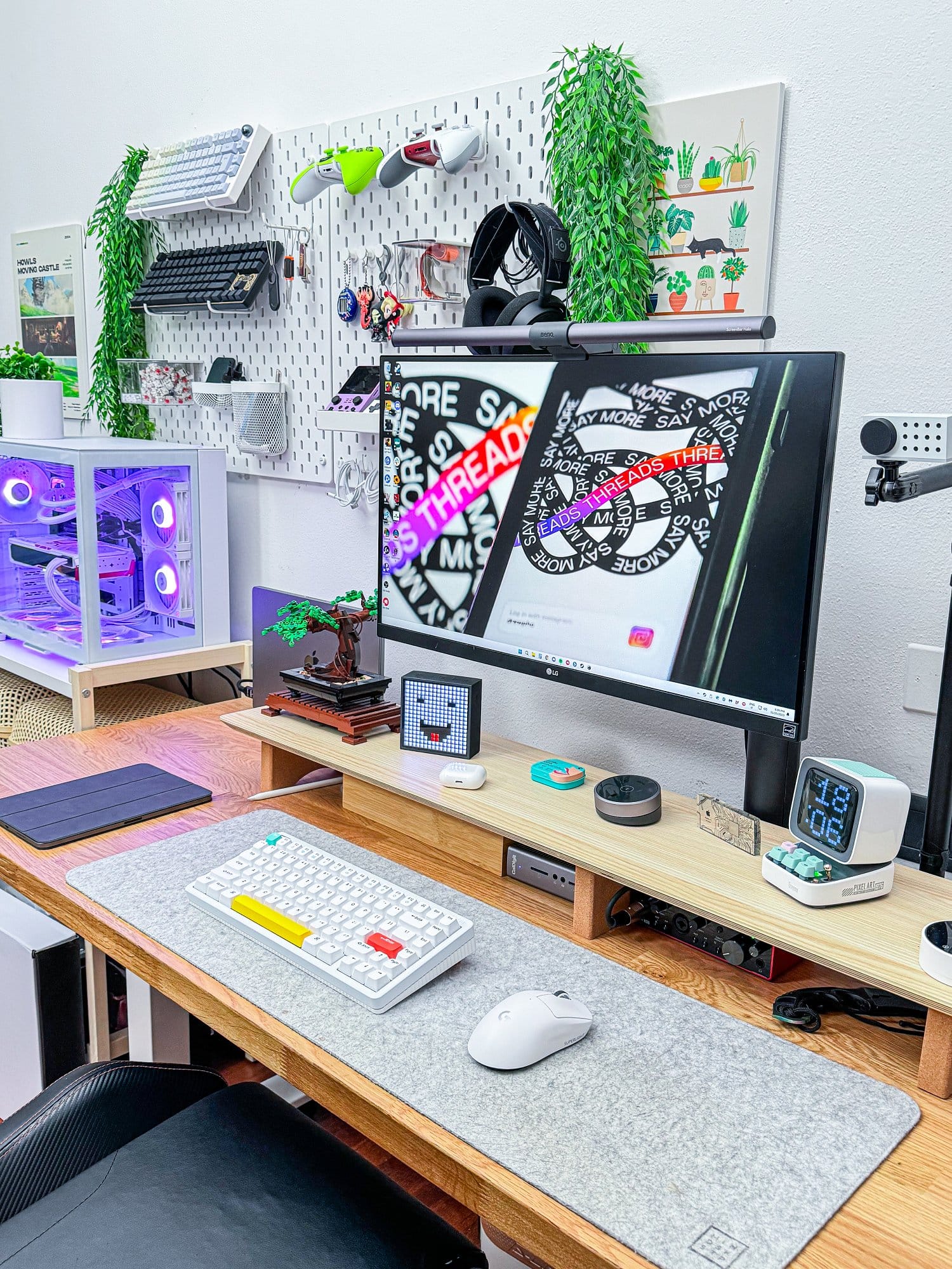 A modern gaming and work setup featuring an LG 27UN880P monitor, NuPhy Halo keyboard, Logitech G Superlight Pro mouse on a Harber London wool-like desk mat, MacBook Pro M1 Pro 2022, and Radeon 7900XTX external GPU, all arranged on an IKEA KARLBY tabletop with Flexispot legs, with various tech accessories and plants adorning the wall