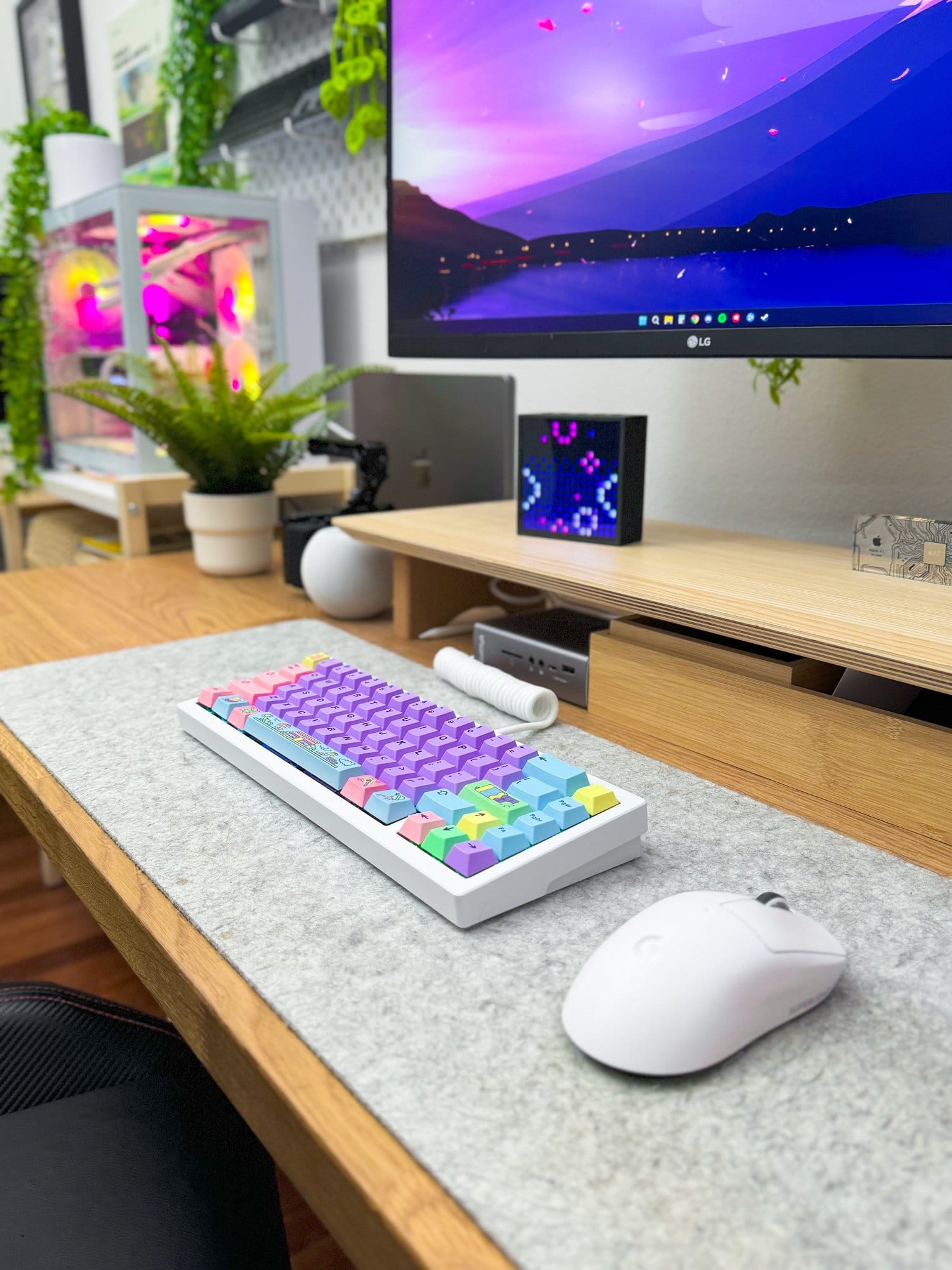 A modern workspace featuring an LG 27UN880P monitor, a colourful NuPhy Halo keyboard, Logitech G Superlight Pro mouse on a Harber London wool-like desk mat, MacBook Pro M1 Pro 2022, and a glowing PC setup with Radeon 7900XTX external GPU, complemented by decorative plants and tech accessories