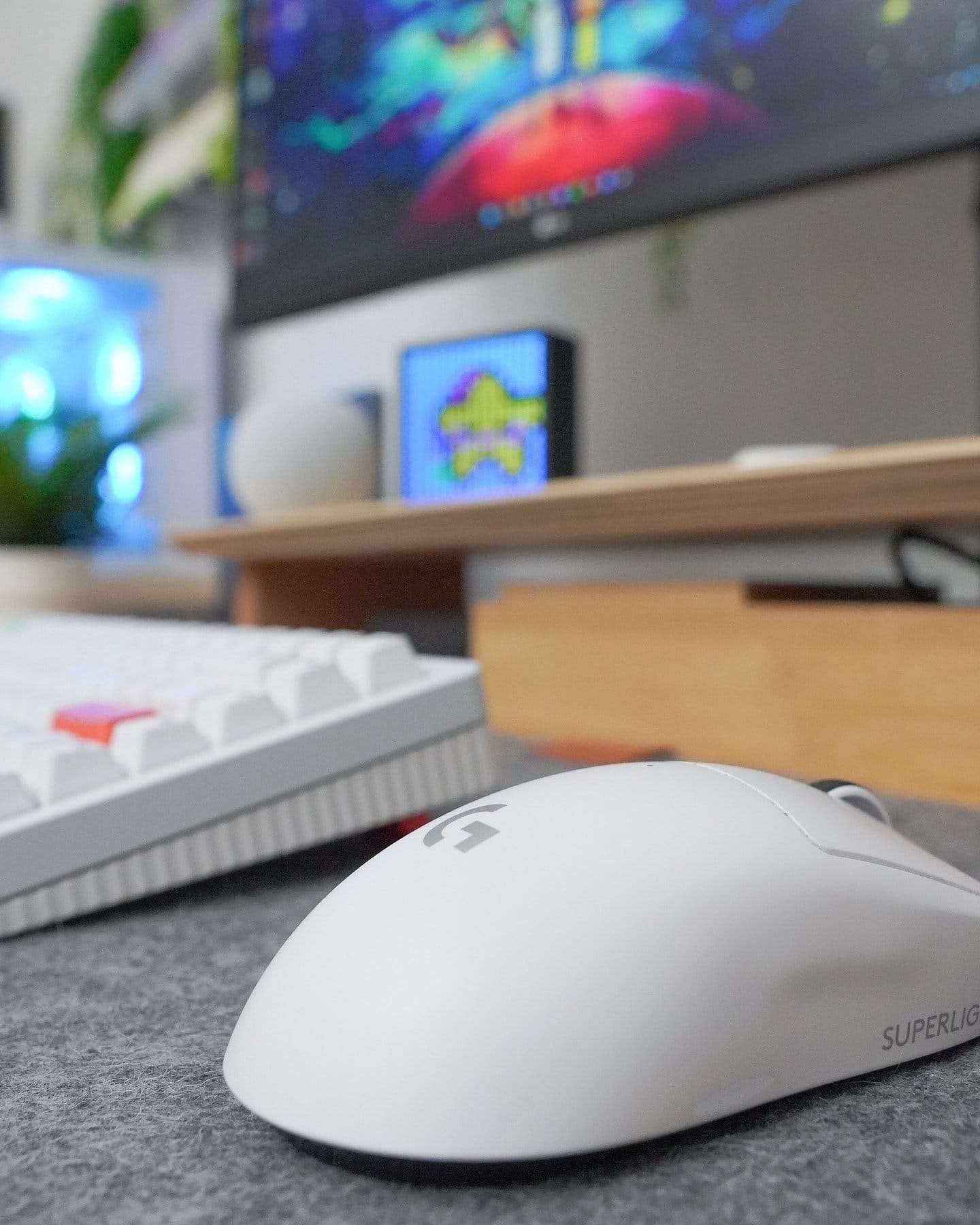 A close-up view of a Logitech G Superlight Pro mouse on a Harber London wool-like desk mat, with a NuPhy Halo keyboard and part of an LG 27UN880P monitor in the background, showcasing a vibrant and colourful display