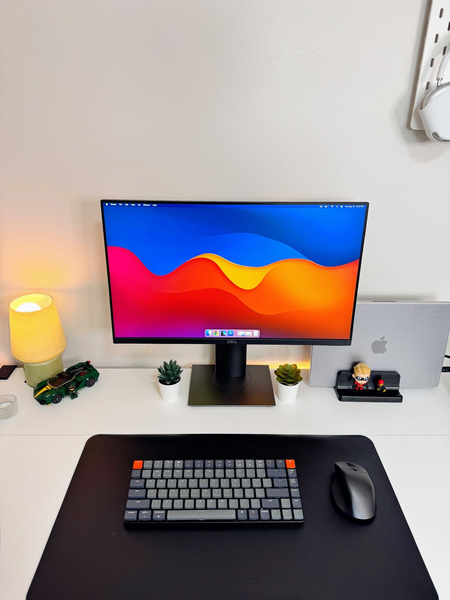 A close-up of a neat desk setup with a Dell P2419H monitor, Keychron K3 wireless mechanical keyboard, and Keychron M3 mouse, surrounded by small decor items like two potted IKEA FEJKA plants