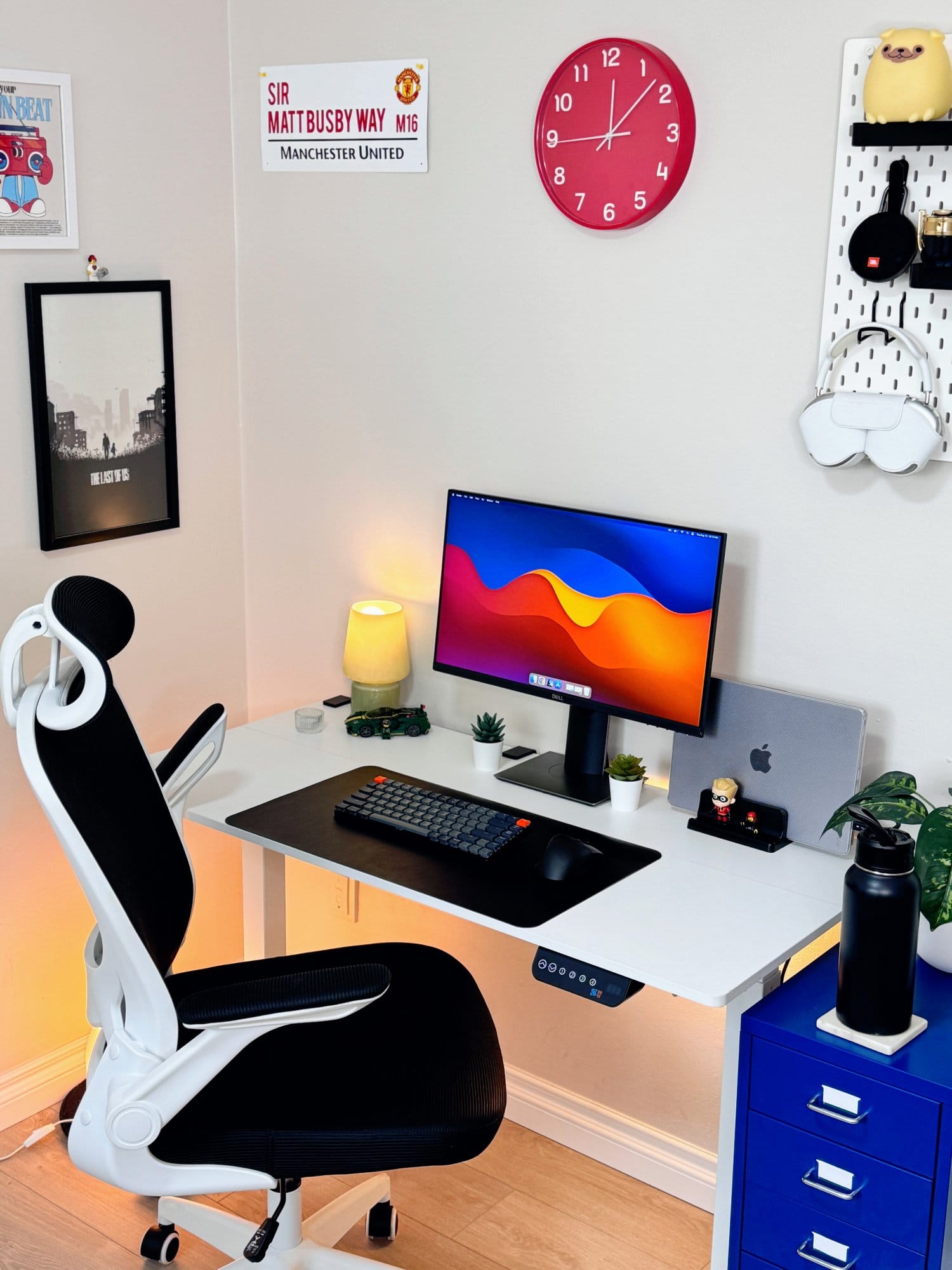 A clean and organised workspace with a Dell P2419H monitor, MacBook Pro 2023, and Keychron K3 mechanical keyboard on a SHW adjustable desk, paired with a KERDOM ergonomic chair, pink clock, Manchester United wall sign, and various decor items