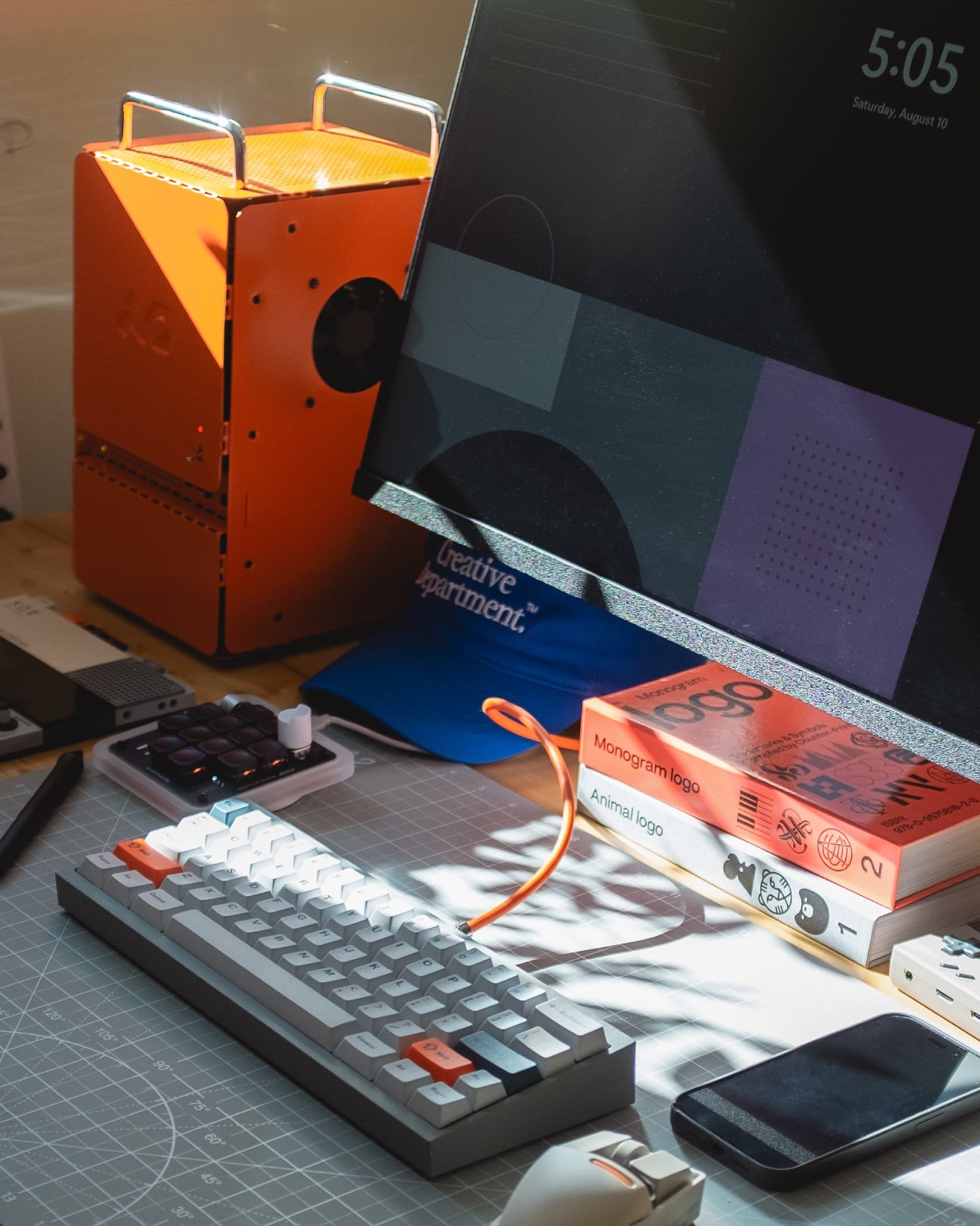 A well-lit desk setup with a custom-built keyboard with orange accents, a Computer-1 (TE) case, a Wacom Cintiq 22HD tablet, and a Work Louder macropad