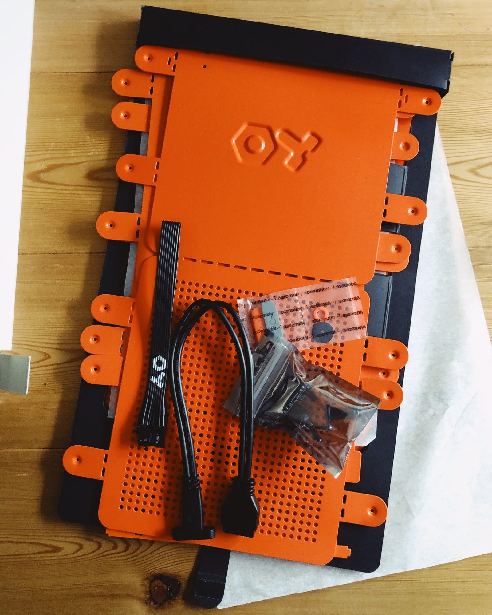  An unassembled orange Computer-1 (TE) PC case lays flat on a wooden surface, with its metal panels, screws, and cables neatly arranged, ready for assembly