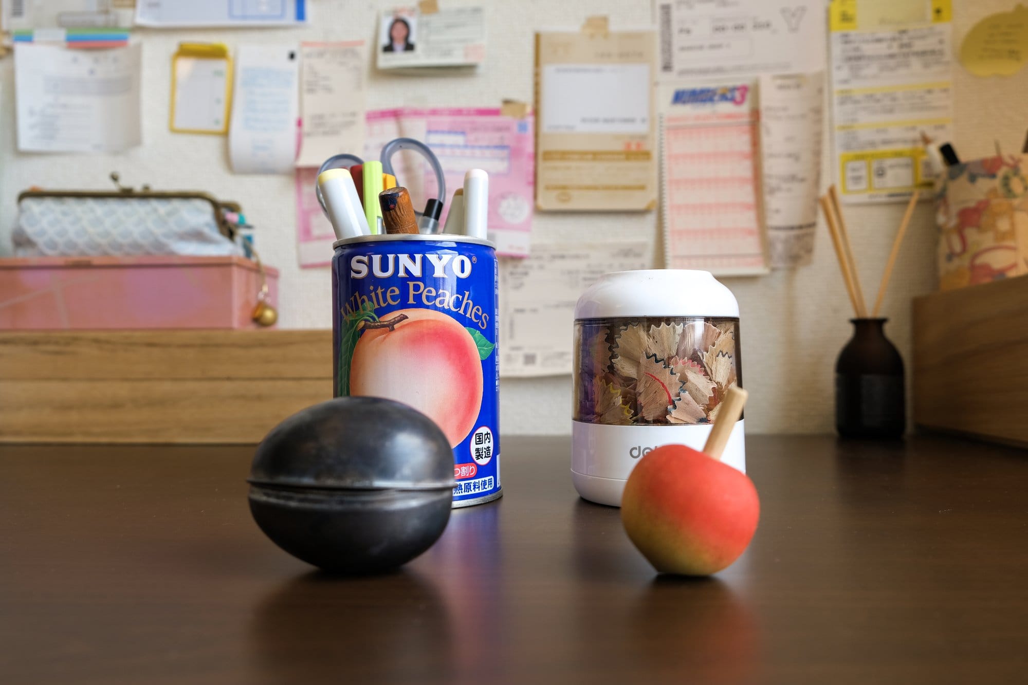 A desk with a peach that can used as a pen holder, an electric pencil sharpener, a small wooden peach-shaped spinning top, and an egg-shaped metal mould