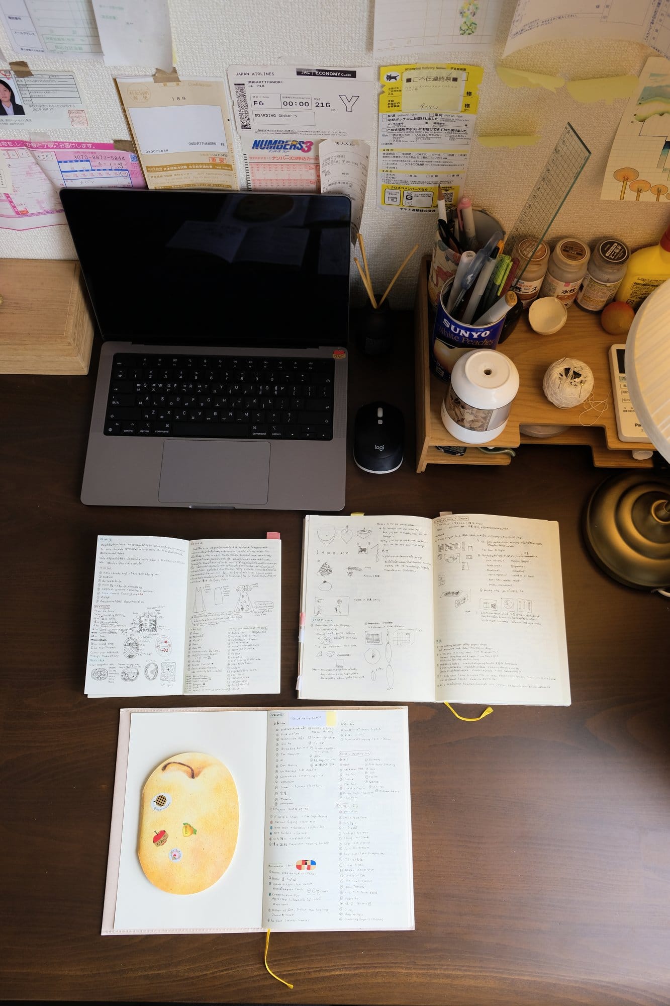 A tidy desk setup with an open MacBook Pro, a Logitech mouse, and several notebooks filled with notes and drawings