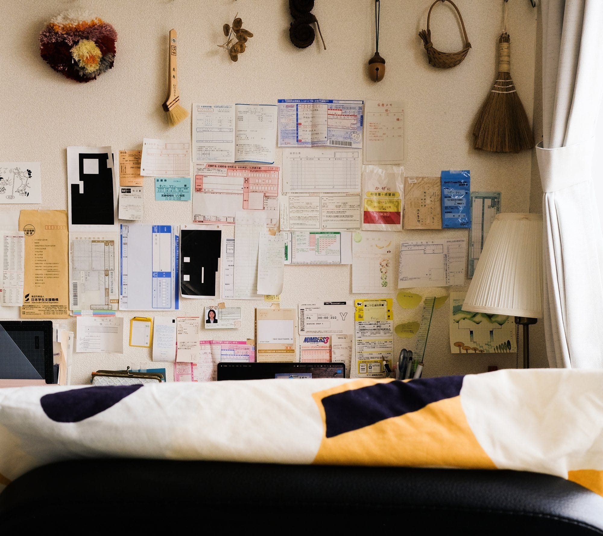 A workspace wall covered in neatly arranged documents and notes, with a broom and decorative items hanging above, partially visible behind a chair