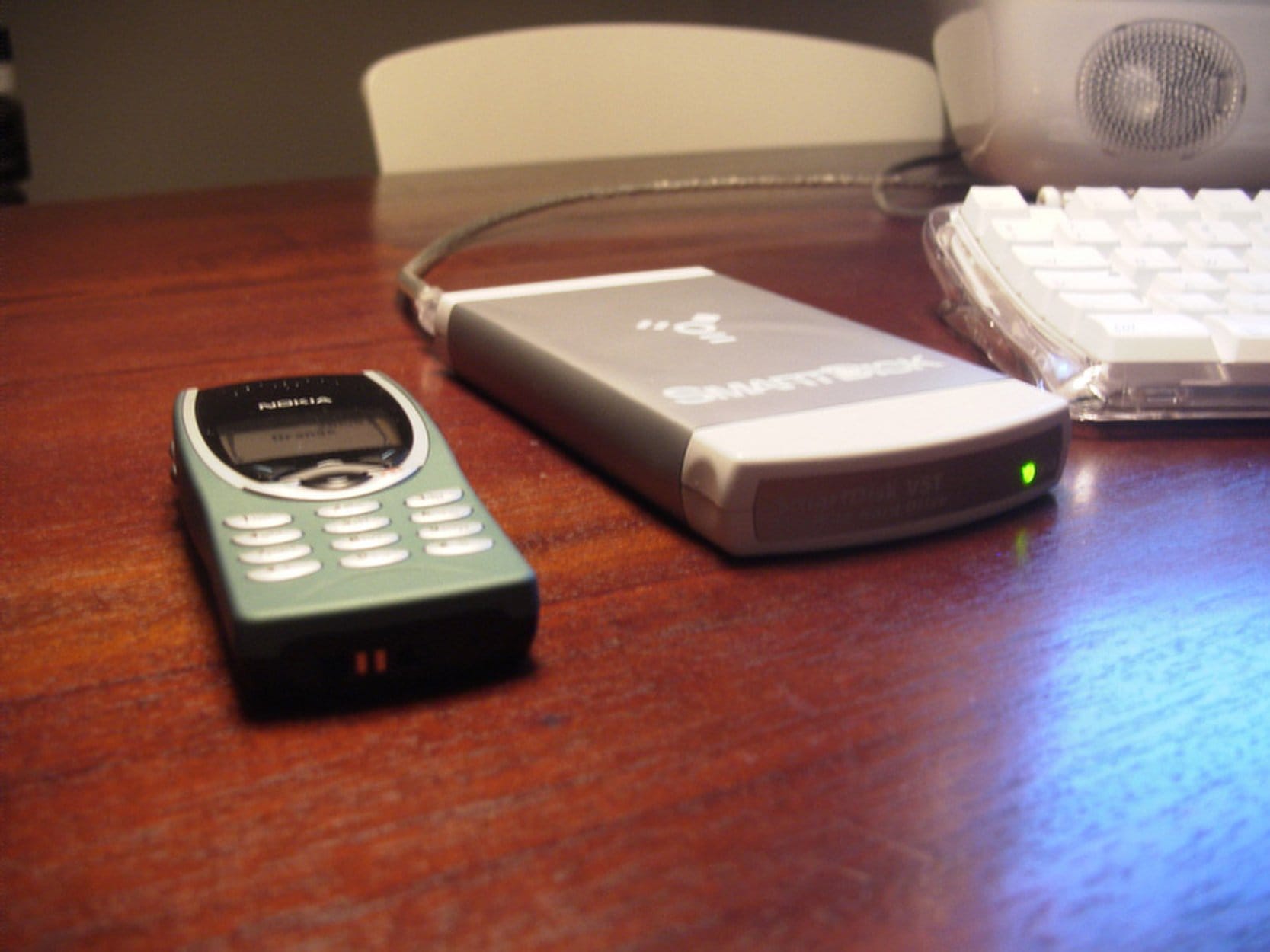 A Nokia mobile phone and a SmartDisk VST portable hard drive sit on a wooden desk next to an Apple keyboard