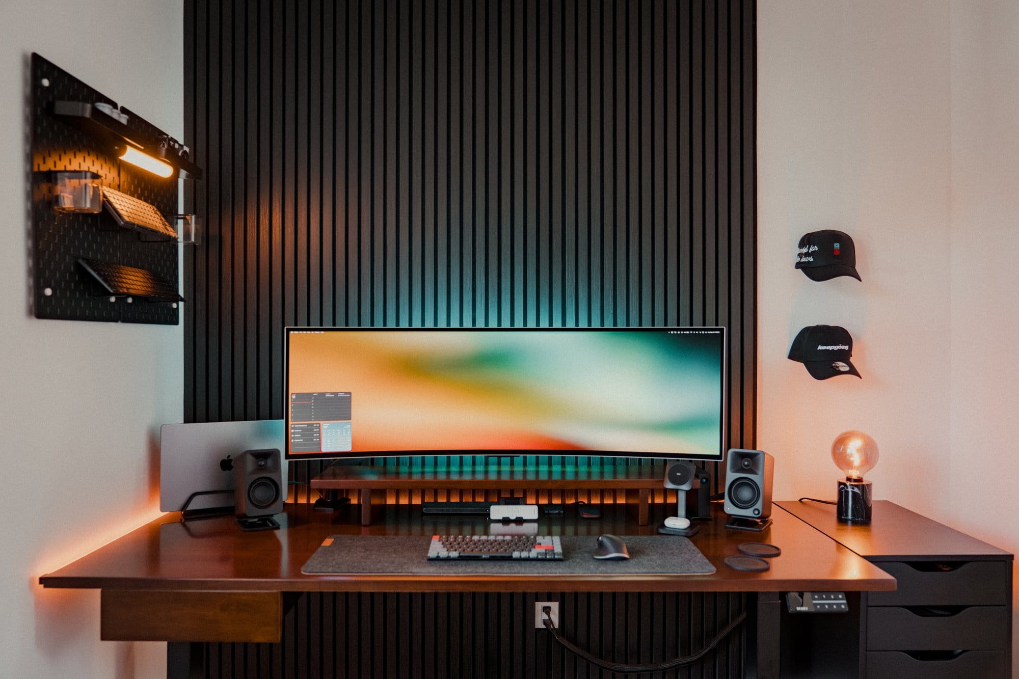 A home office setup with a Samsung 49″ Odyssey OLED G9 monitor, MacBook Pro M1 Max, Kanto ORA Reference Desktop Speakers, Keychron K3 Pro keyboard, and IKEA SKÅDIS pegboard mounted on the wall