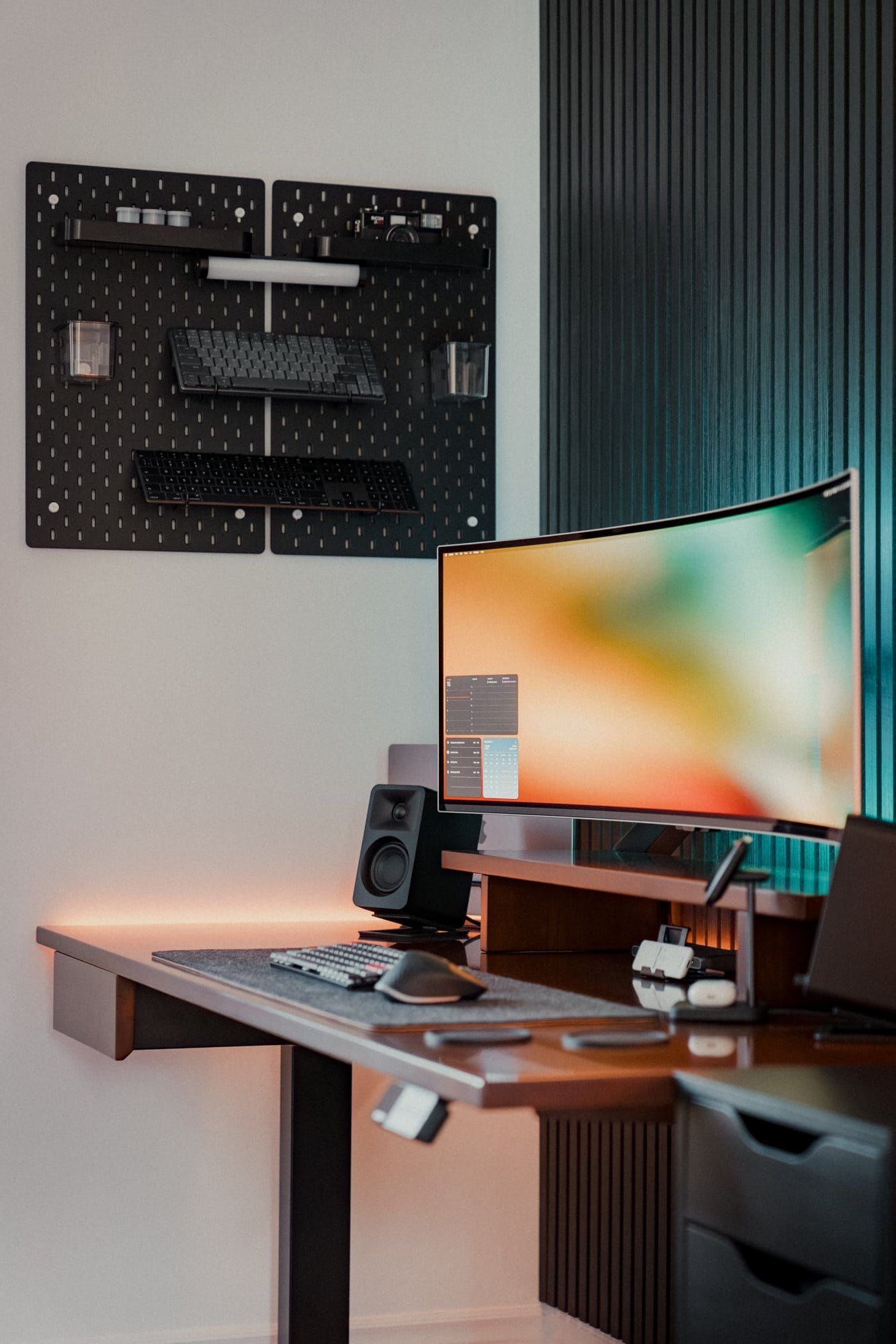 A home office setup showing a Samsung 49″ Odyssey OLED G9 monitor, Kanto ORA Reference Desktop Speakers, and an IKEA SKÅDIS pegboard mounted on the wall, holding keyboards and various accessories