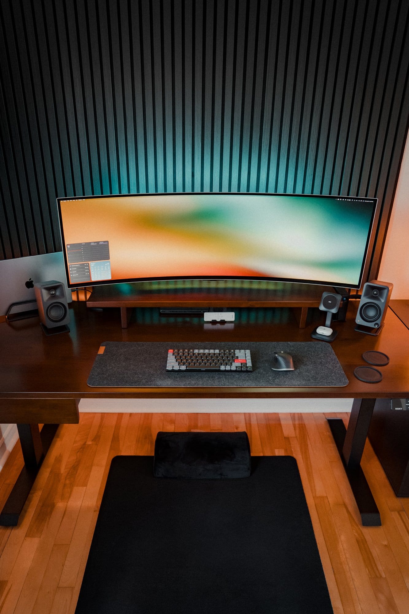 A desk setup with a Samsung 49″ Odyssey OLED G9 monitor, Keychron K3 Pro keyboard on a Desky Cork and Felt Desk Pad, Kanto ORA Reference Desktop Speakers, and a MacBook Pro M1 Max to the side