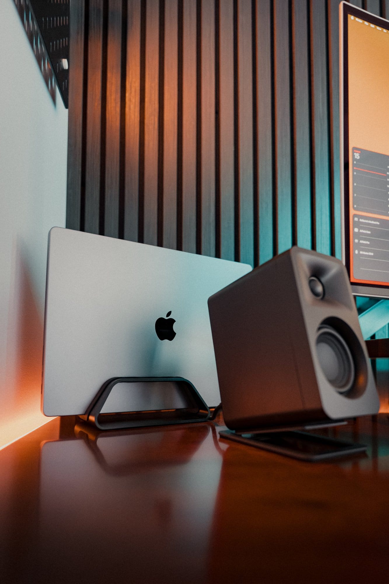 Close-up of a MacBook Pro M1 Max placed in a HumanCentric Vertical Laptop Stand next to a Kanto ORA Reference Desktop Speaker