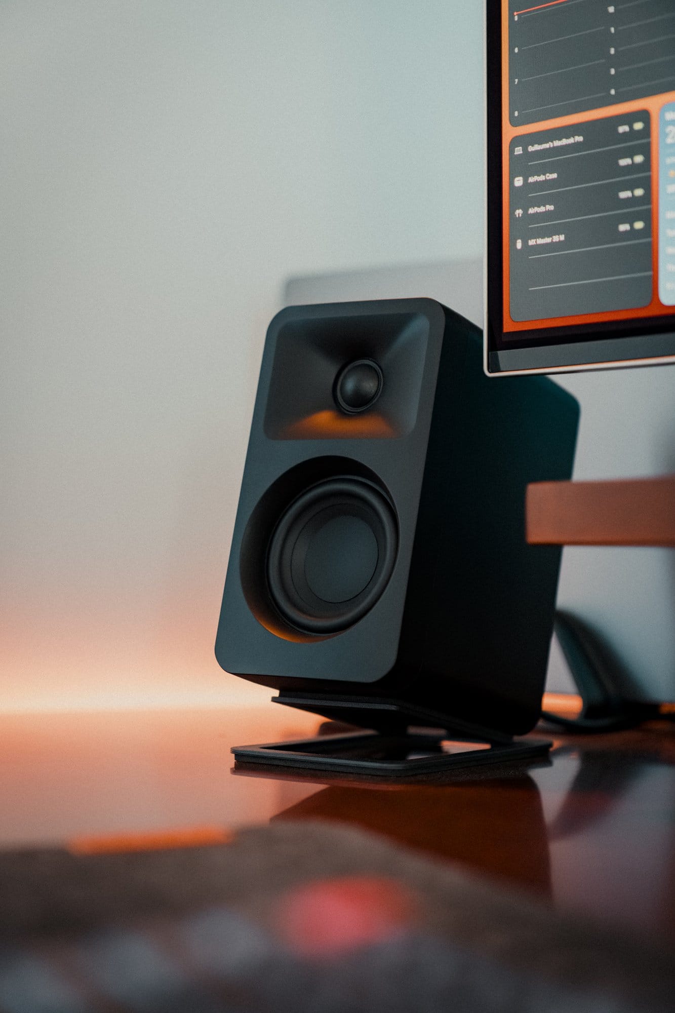 Close-up of a Kanto ORA Reference Desktop Speaker on a Kanto S2 Desktop Speaker Stand next to a monitor