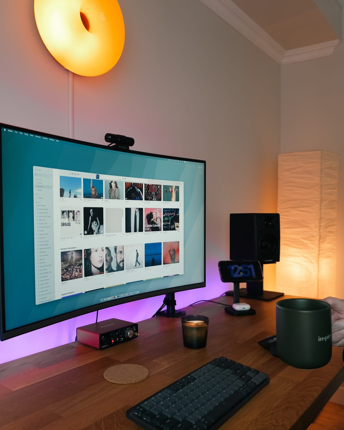 A desk setup with a Samsung LU32R590CWNXZA monitor, a Logitech MX Mechanical Mini keyboard, and a Focusrite audio interface on an IKEA KARLBY oak surface, alongside a green mug, candle, and M-Audio AV32 speaker beneath an IKEA VARMBLIXT wall lamp