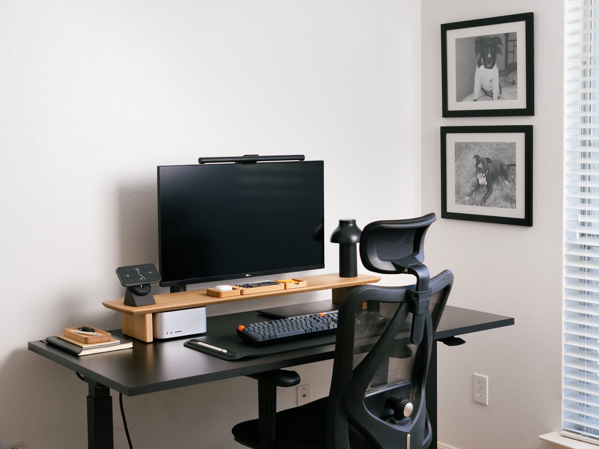 A workspace setup with an LG UltraFine display, a Modhaus desk shelf holding a Hay PC portable lamp and organisation trays, a Keychron K10 keyboard, and framed dog portraits on the wall