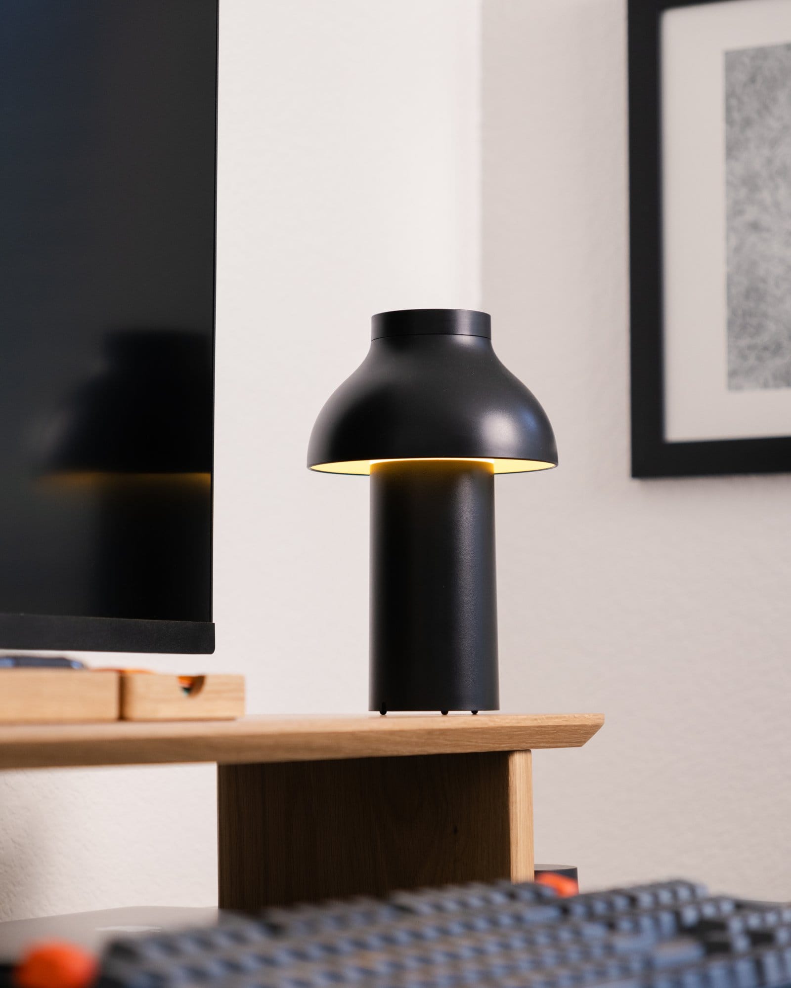 A Hay PC portable lamp placed on a Modhaus desk shelf, with part of a Keychron K10 keyboard and a monitor visible in the foreground