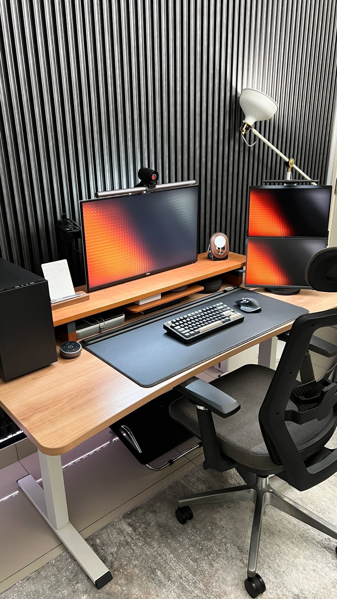 A home office desk setup arranged on a Tyyli standing desk with a Lone Birch desk shelf, an ergonomic chair, and a task lamp