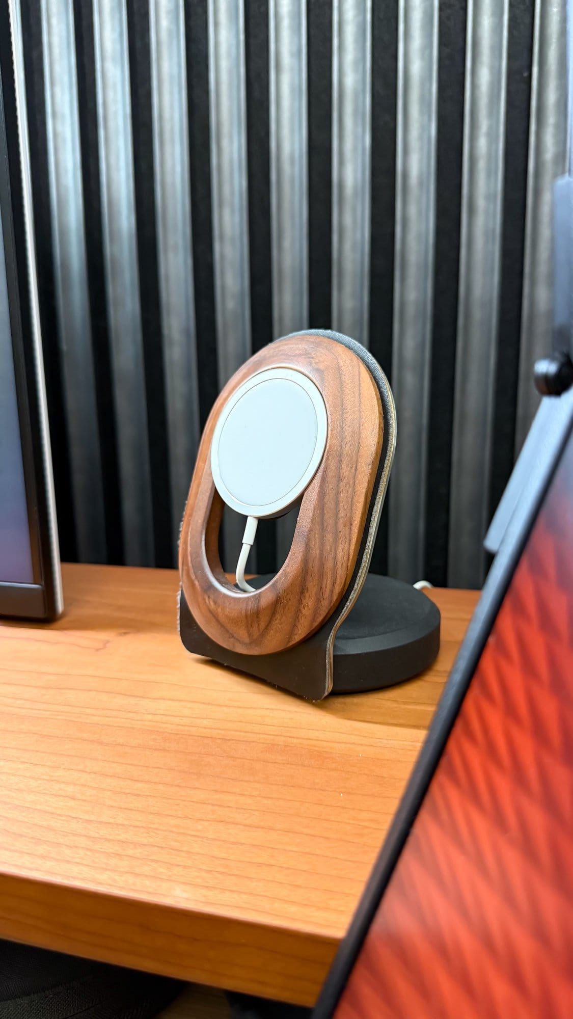 A close-up of a wooden Mysetup MagSafe charging holder positioned on a desk shelf, set against a Reforma acoustic panel backdrop