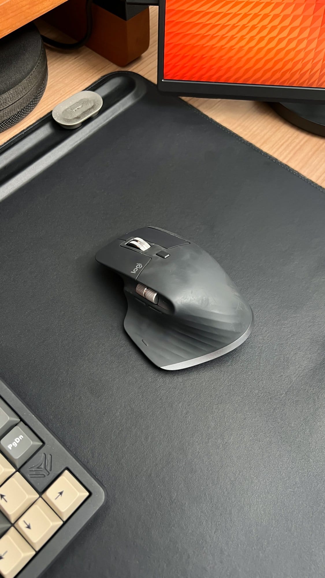 A close-up of a Logitech MX Master 3 mouse on an Orbitkey desk mat, with part of an Elecfox Inky 75 keyboard and a JSAUX FlipGo portable monitor in the background