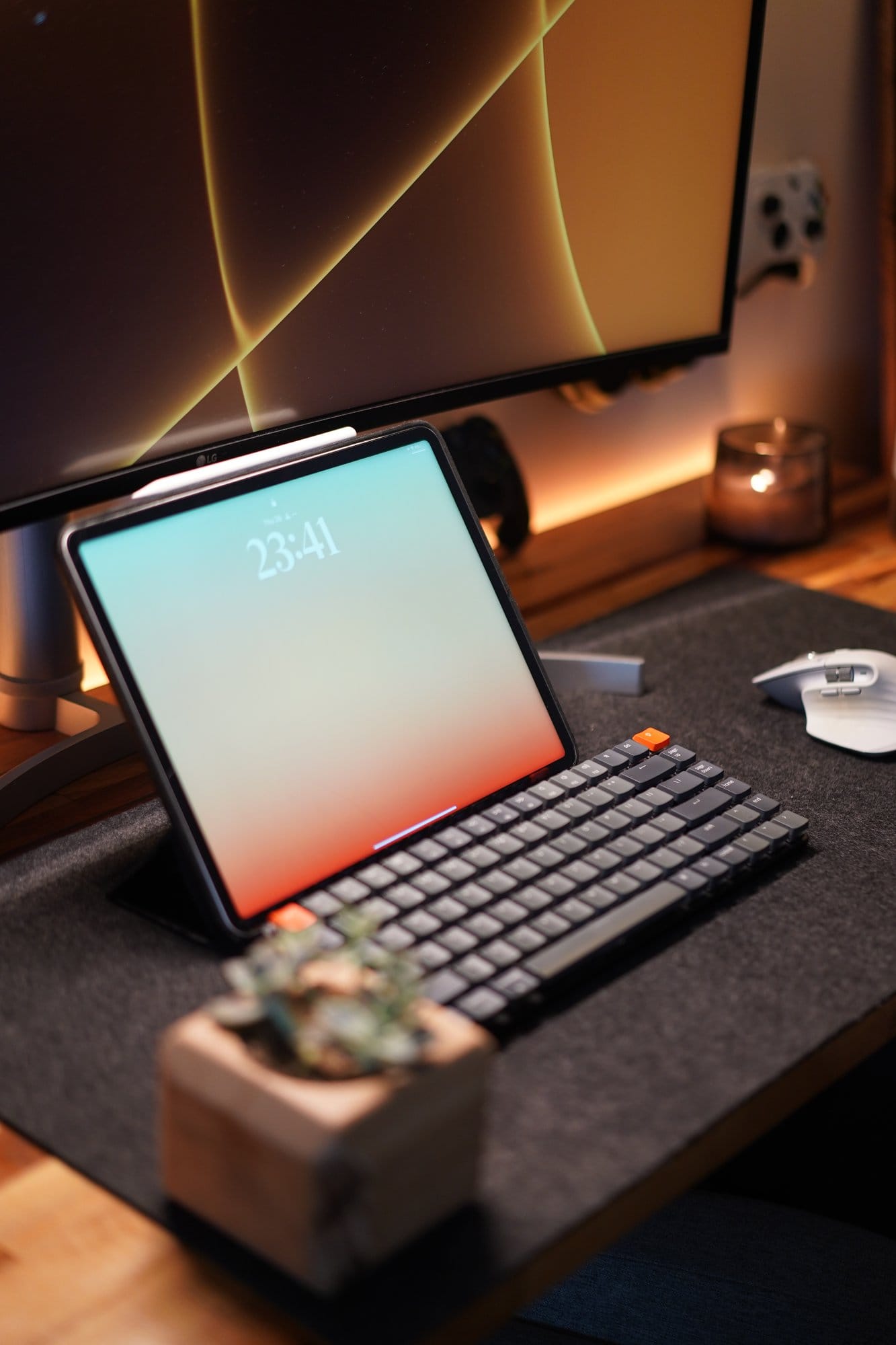 An iPad displaying the time 23:41 rests on a desk setup with a Keychron K3 keyboard and a small wooden planter holding a succulent, with a candle and a monitor in the background