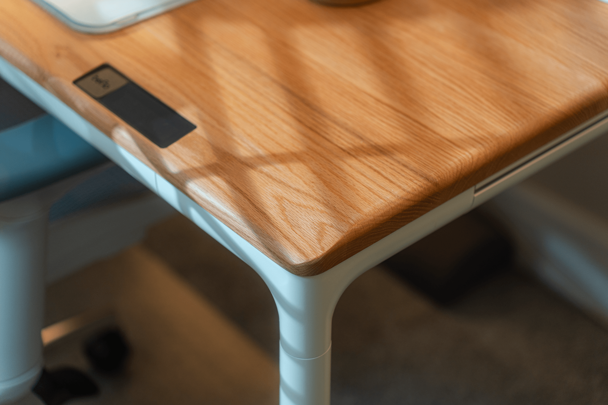 A close-up of a wooden desk with rounded edges, a light grain texture, and a built-in touch control panel on the surface