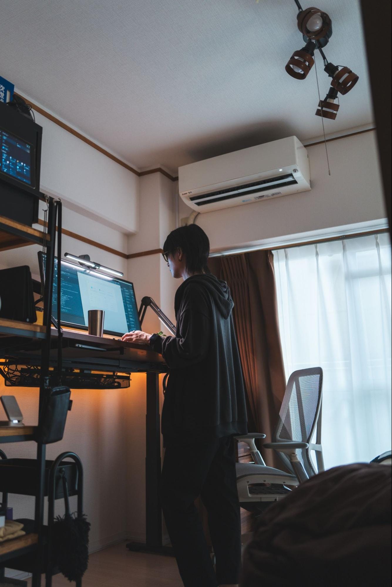  A person standing and working at a Palmwork Elevating Desk with a JAPANNEXT JN-VG34100UWQHDR monitor illuminated by a BenQ ScreenBar Halo, next to a Palmwork chair