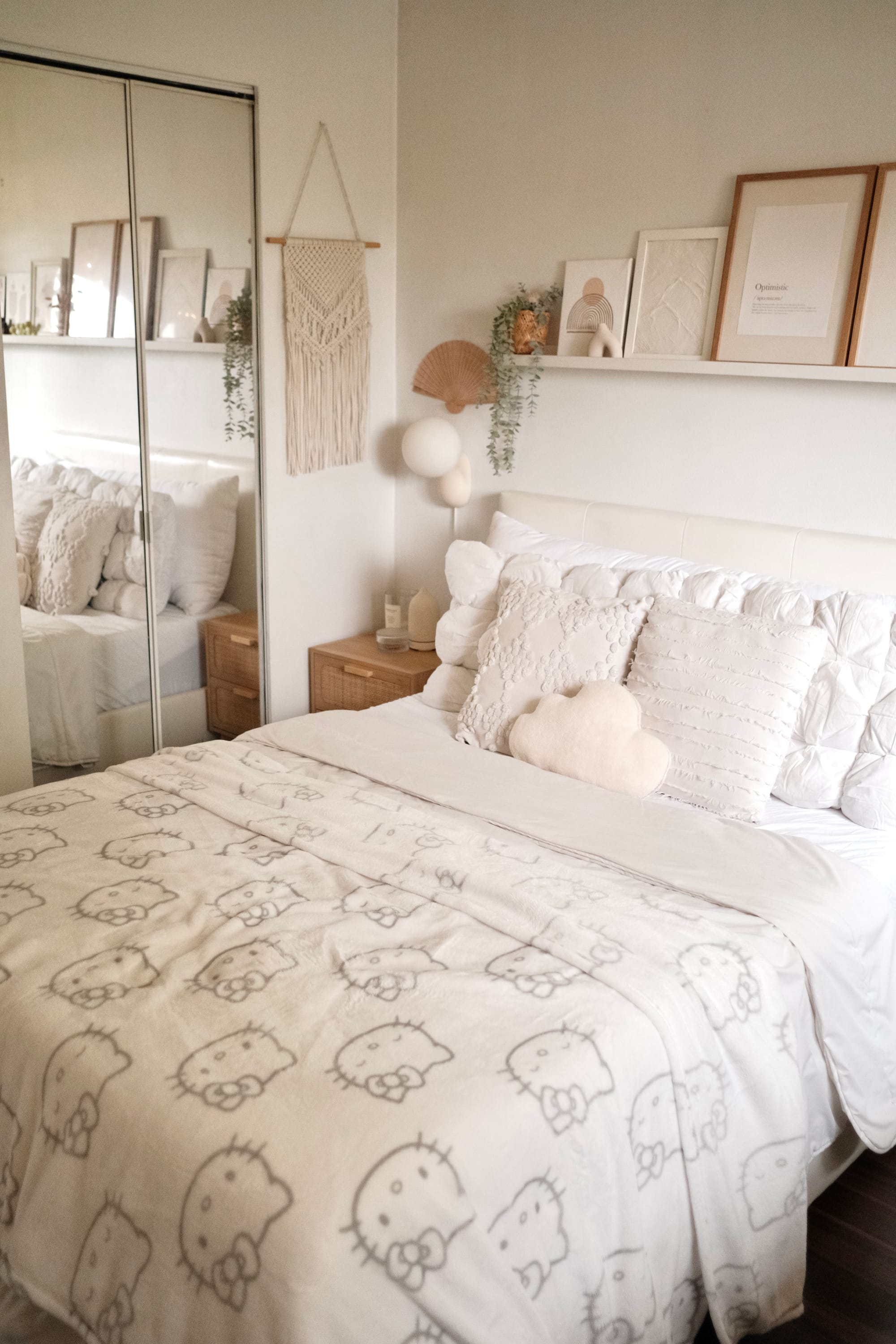 A bed with a Hello Kitty blanket, neutral-toned pillows, and a macramé wall hanging by mirrored closet doors